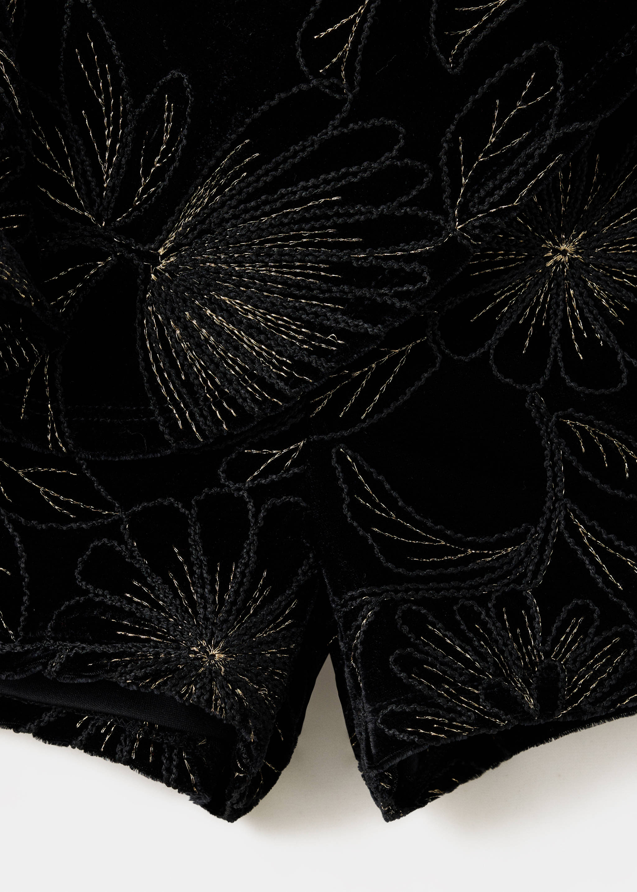 Close-up of black velvet shorts with gold embroidered floral pattern.