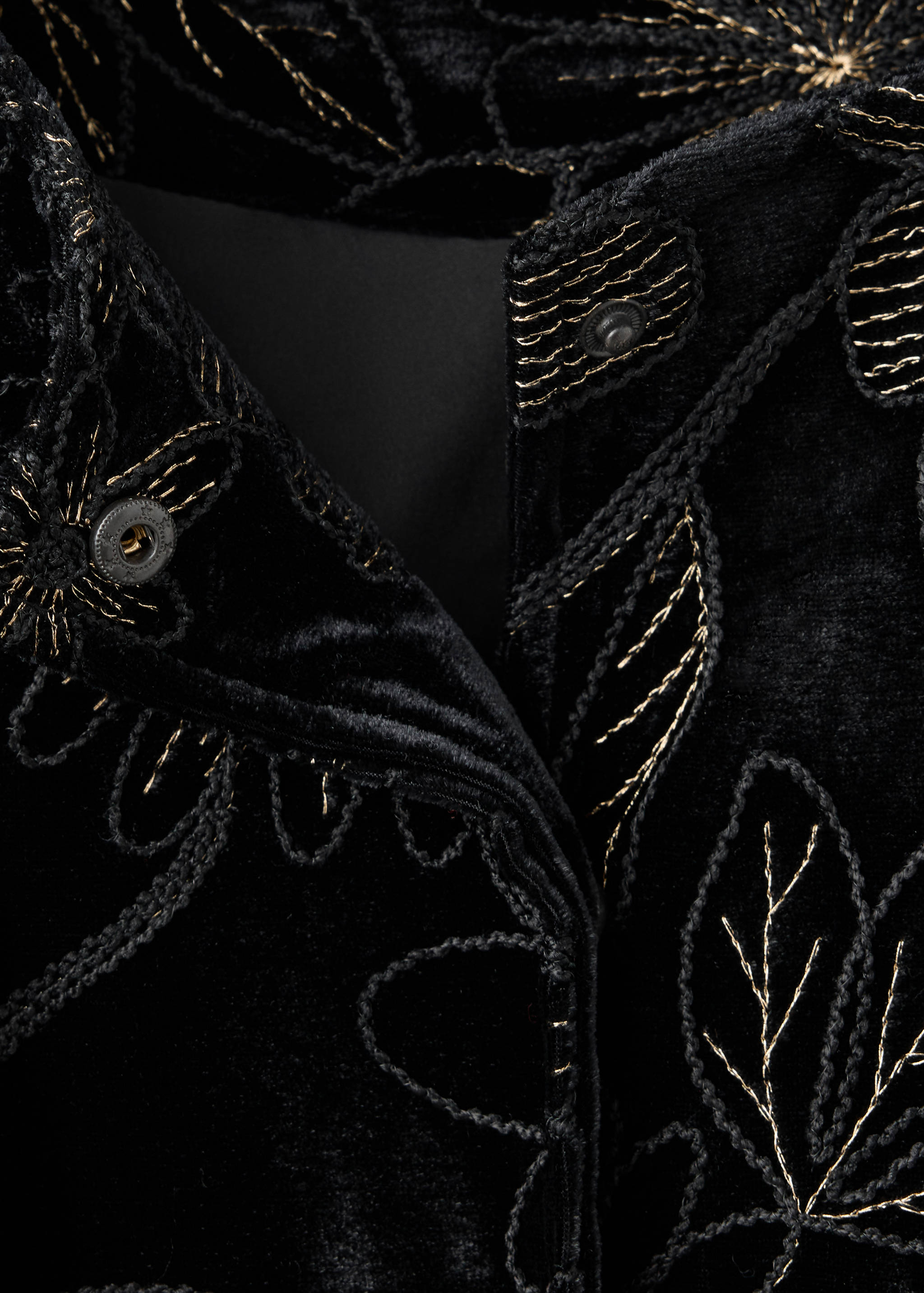 Close-up of a black velvet jacket with metallic gold embroidery and snap buttons.