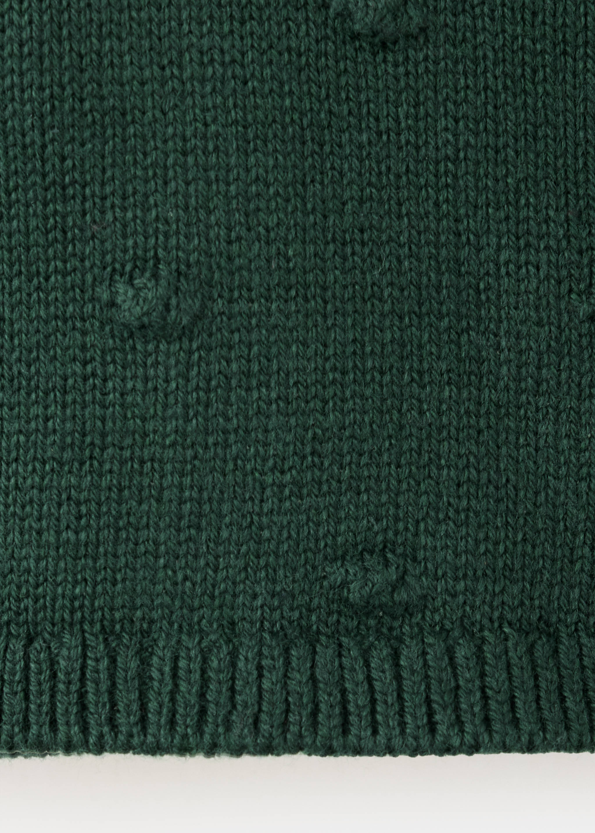 Dark green cardigan fabric close-up showing textured knit and bobbles.