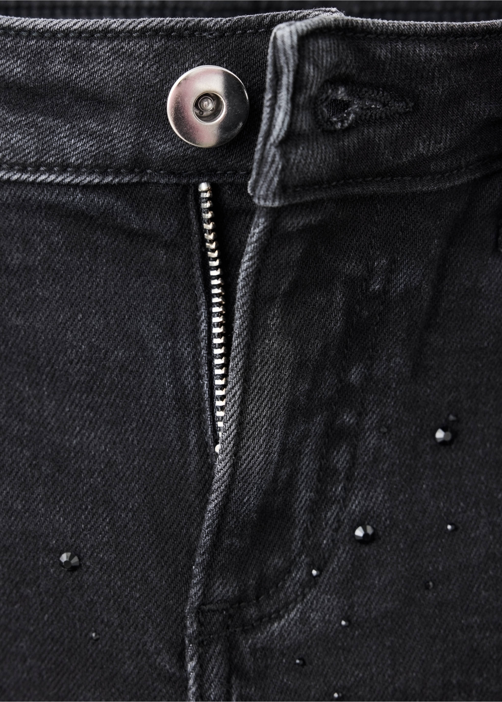 Close-up of the button and zip closure on dark grey rhinestone-embellished denim jeans., Black denim. Ref: 37059228-00.