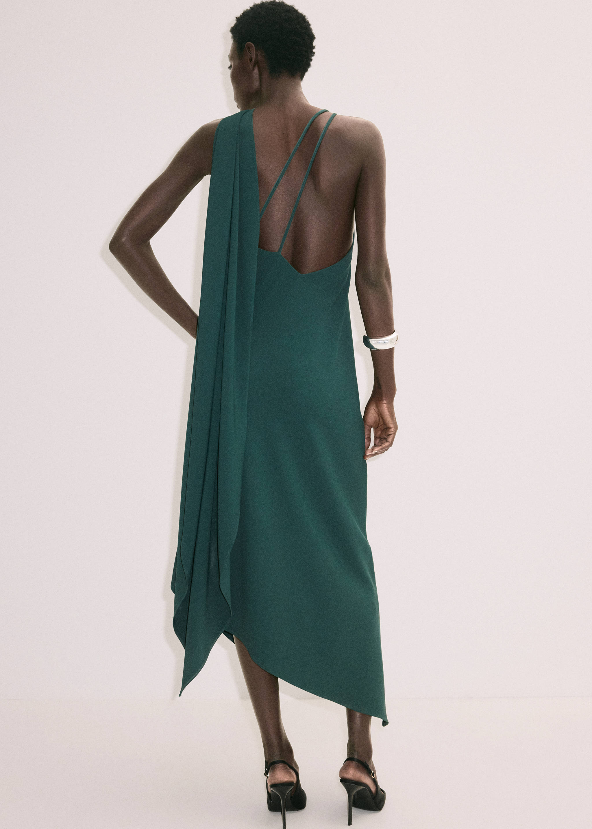 Vestido midi verde oscuro con detalle de capa asimétrica, visto de espaldas.