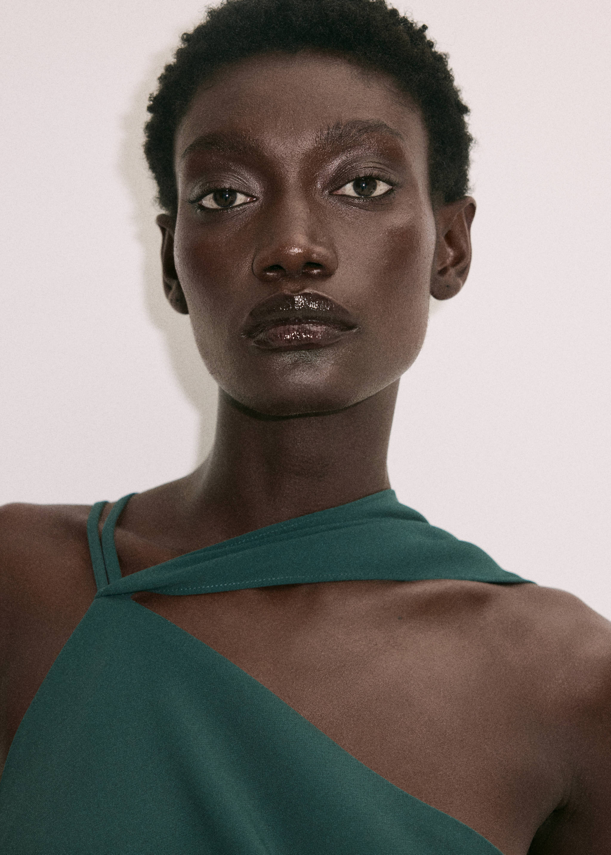 Primer plano de un vestido verde oscuro con escote de tirante asimétrico en una modelo.