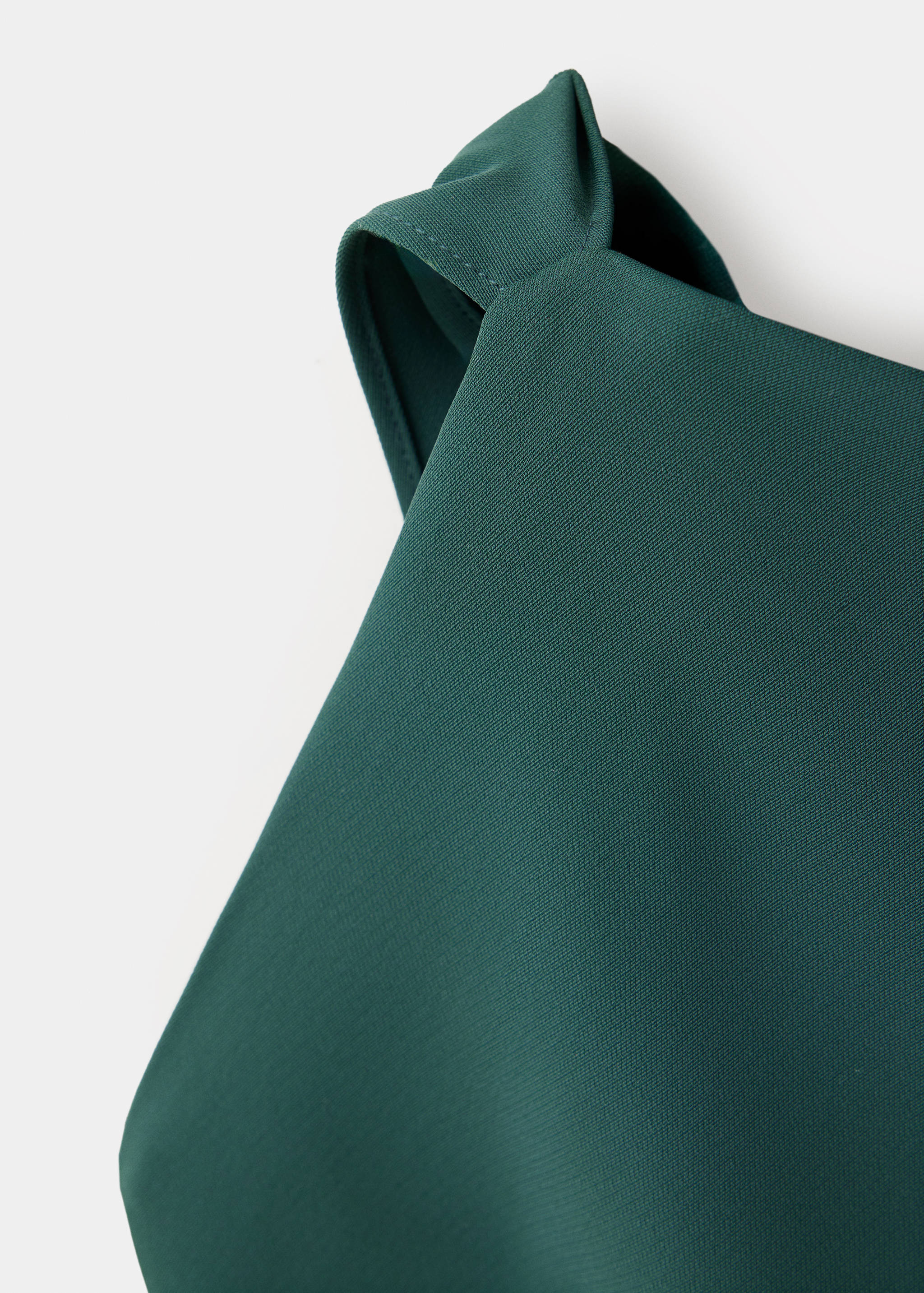 Detalle de la textura del tejido del vestido verde oscuro que muestra el tirante.