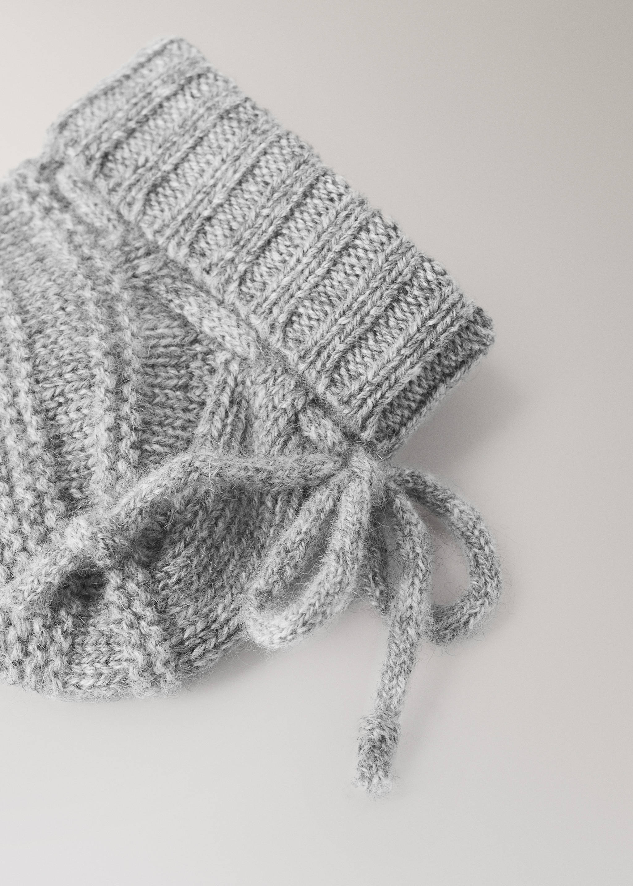 Grey knitted sock with a ribbed cuff and side tie detail.