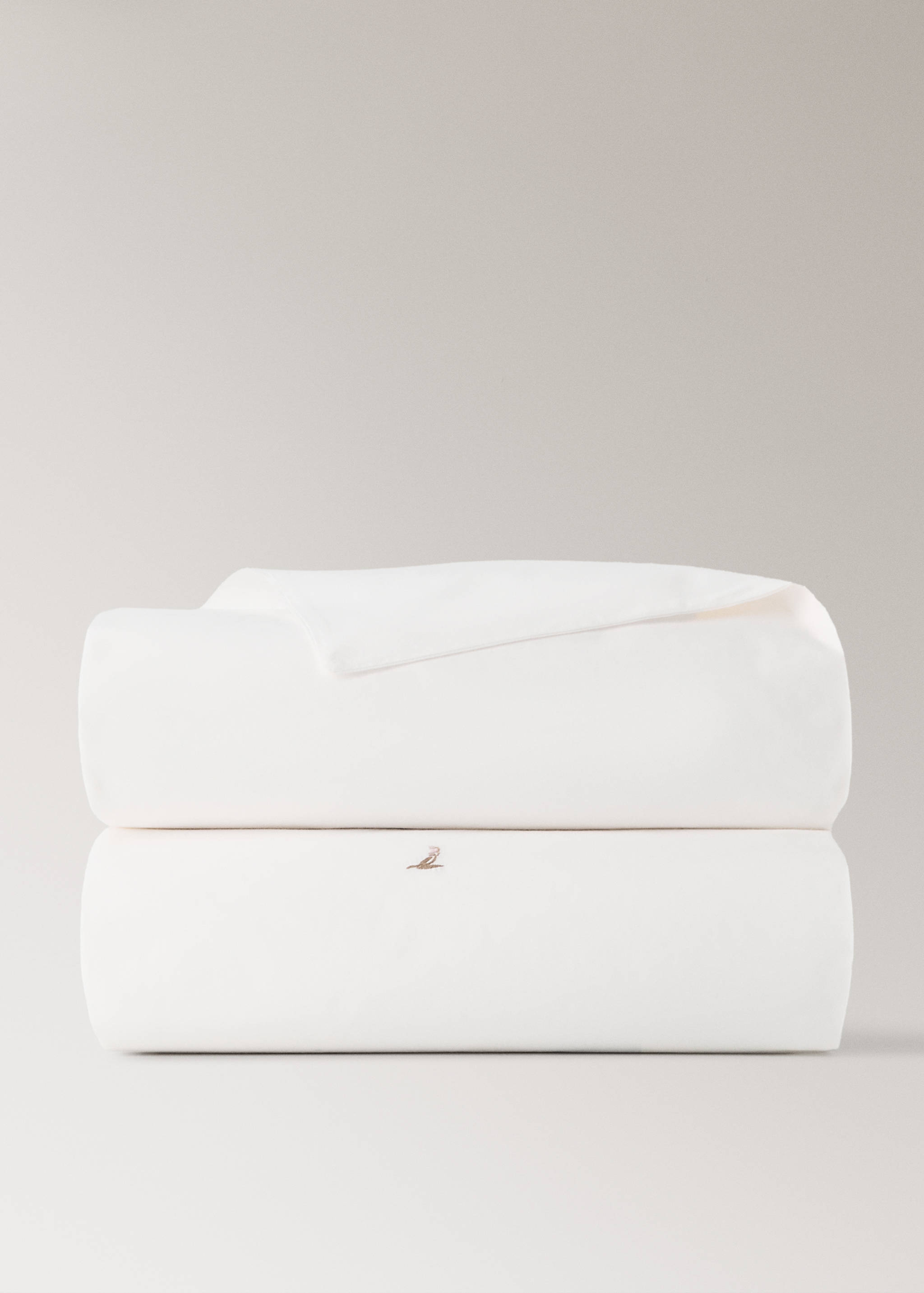 White duvet cover folded in a neat still-life stack with a subtle embroidered bird detail.