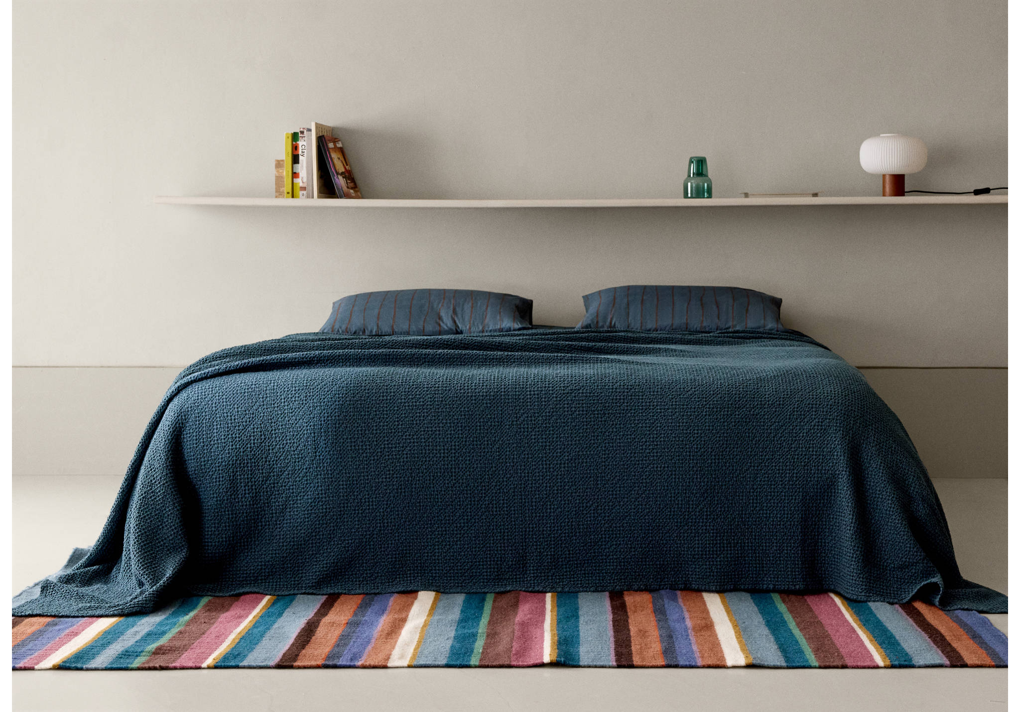 Dark teal textured bedspread on a bed styled with a multi-coloured striped rug.