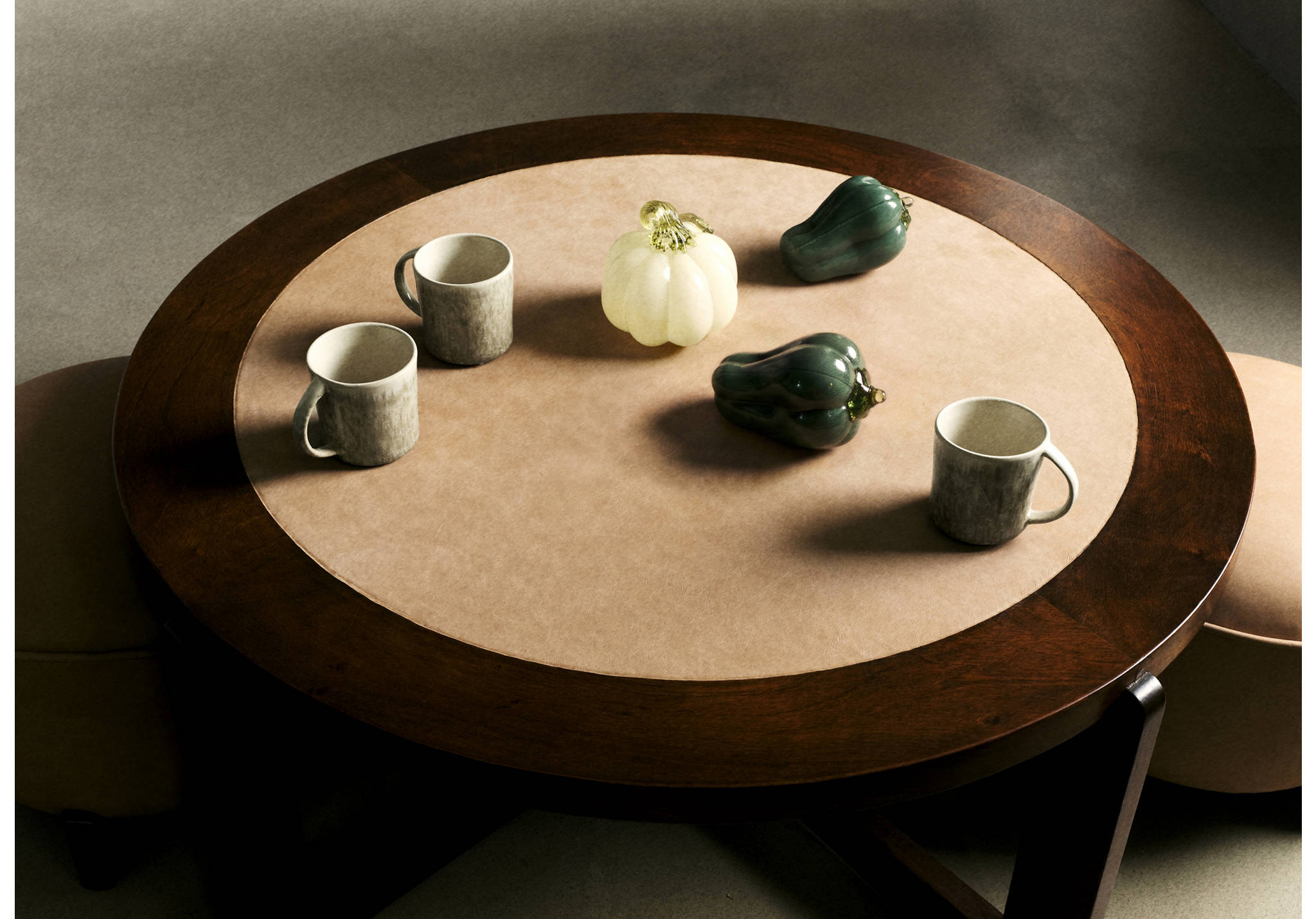 Mesa redonda de madera oscura con artículos de decoración para el hogar que incluyen calabazas de cristal, calabazas y tazas de cerámica.