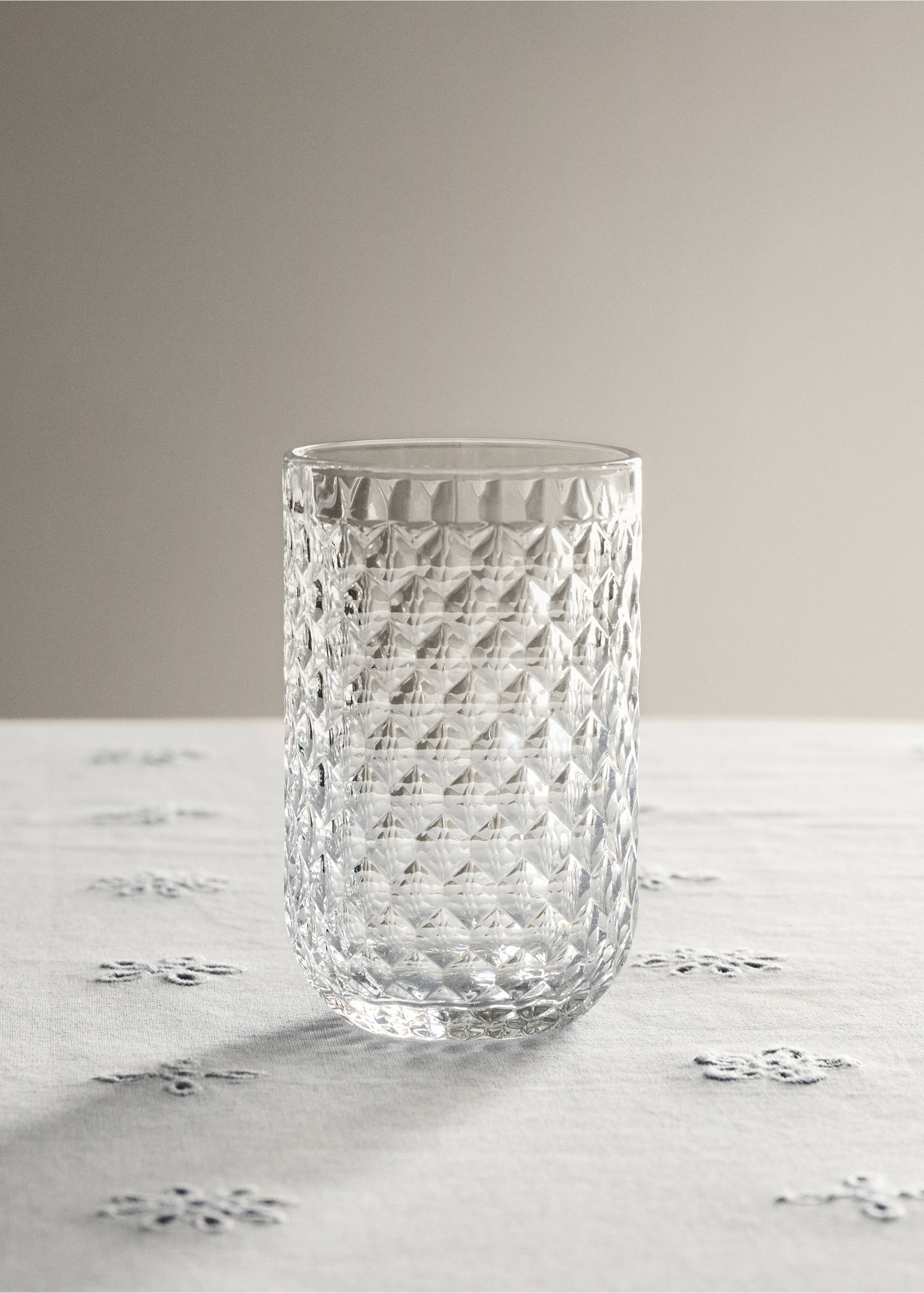 Clear glass tumbler with a textured faceted diamond pattern on a tablecloth., Black. Ref: 37063285-00.