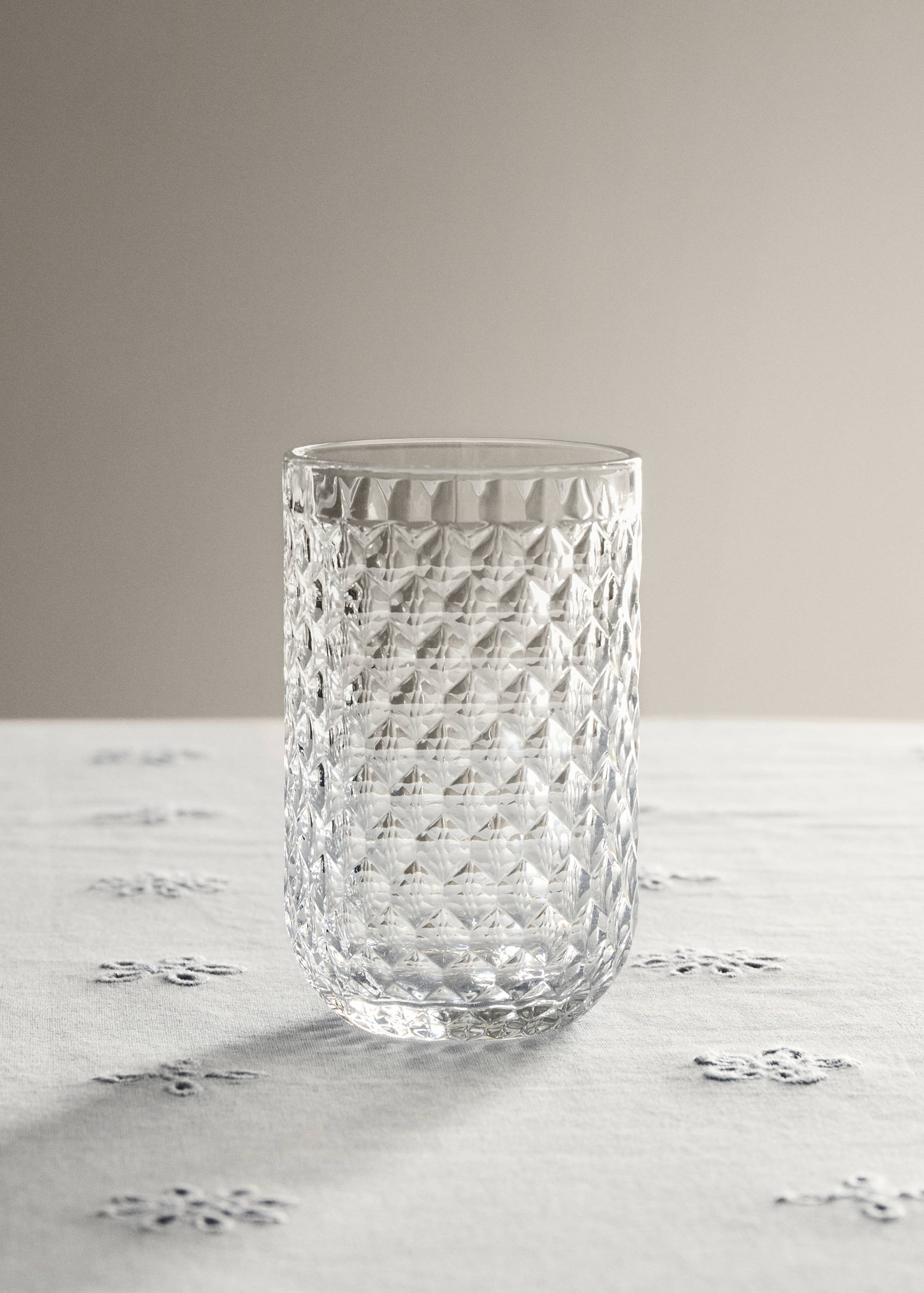 Clear glass tumbler with a textured faceted diamond pattern on a tablecloth.