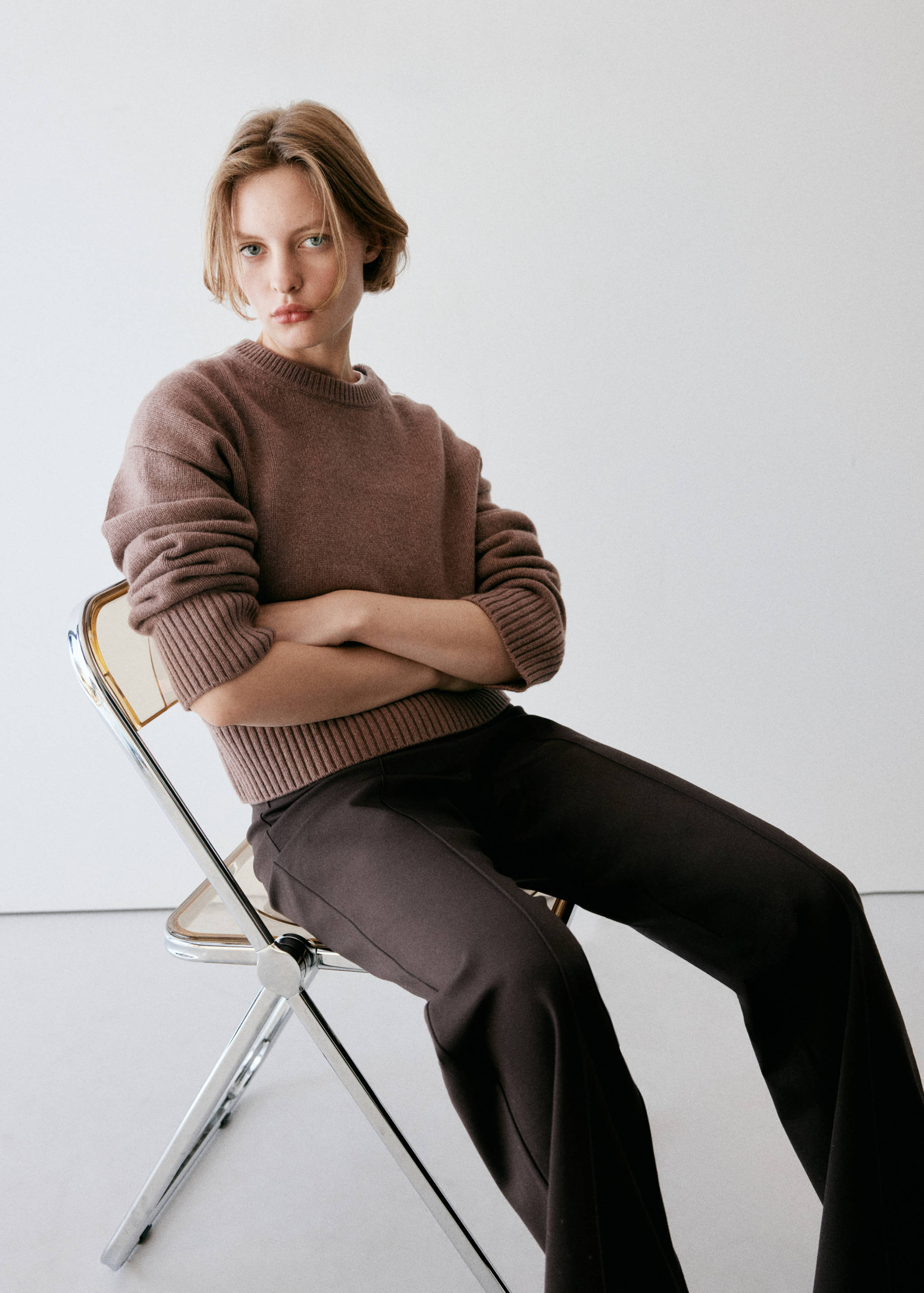 Dark brown trousers worn with a brown crew-neck knitted jumper.
