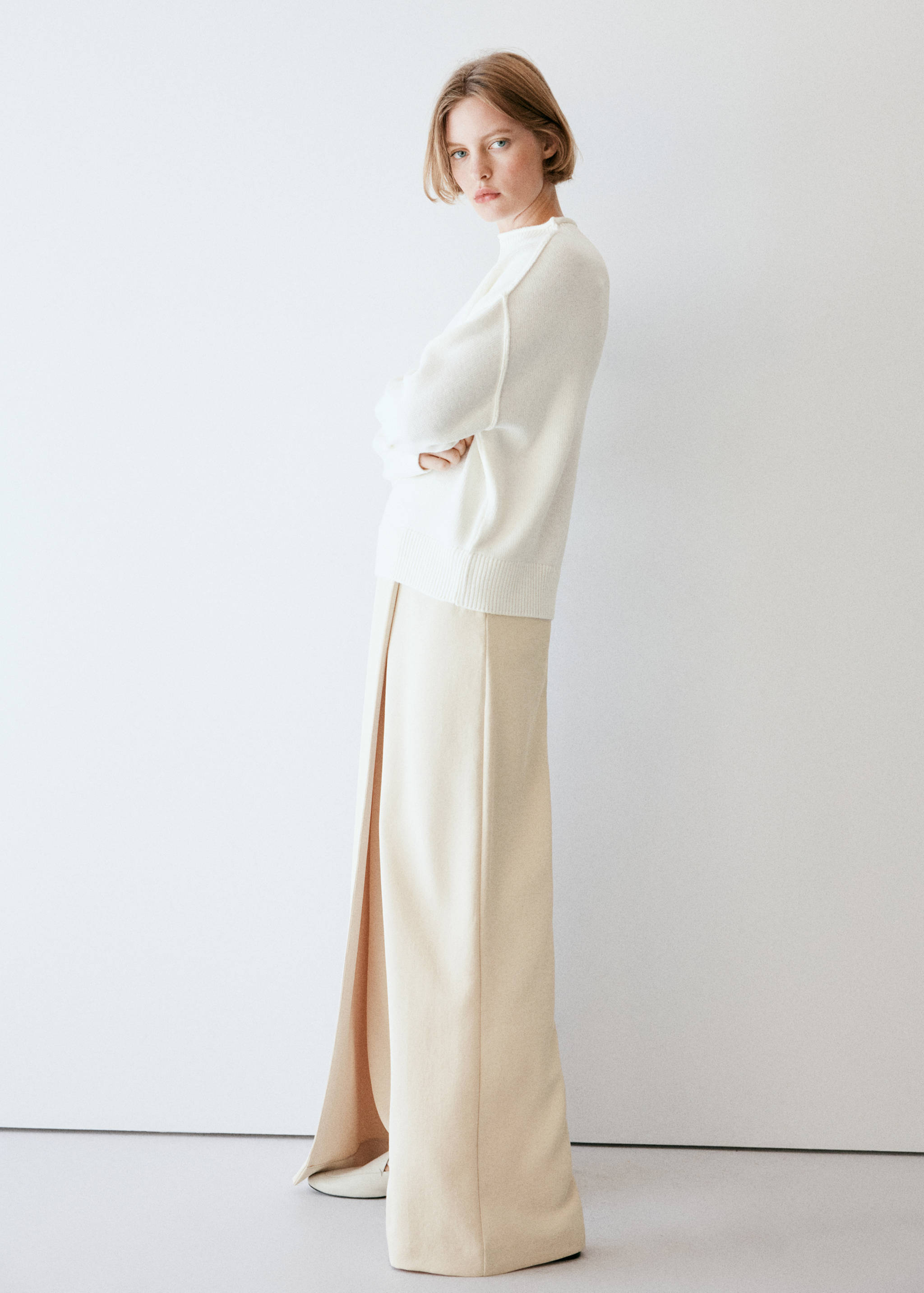 Pale beige wide-leg trousers with a front overlay, worn with a white sweater.