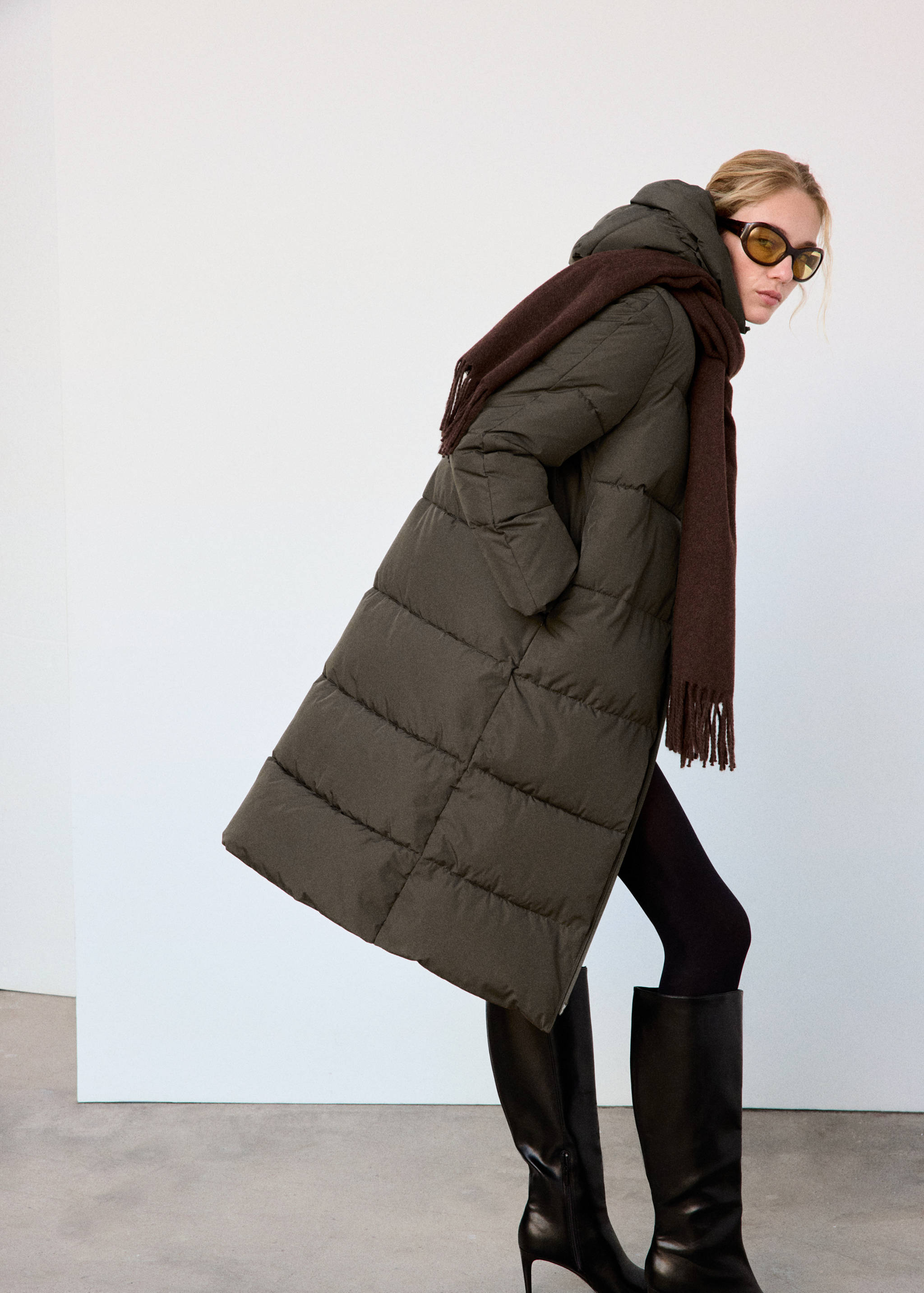 Long dark green quilted anorak with a hood and a dark brown scarf.
