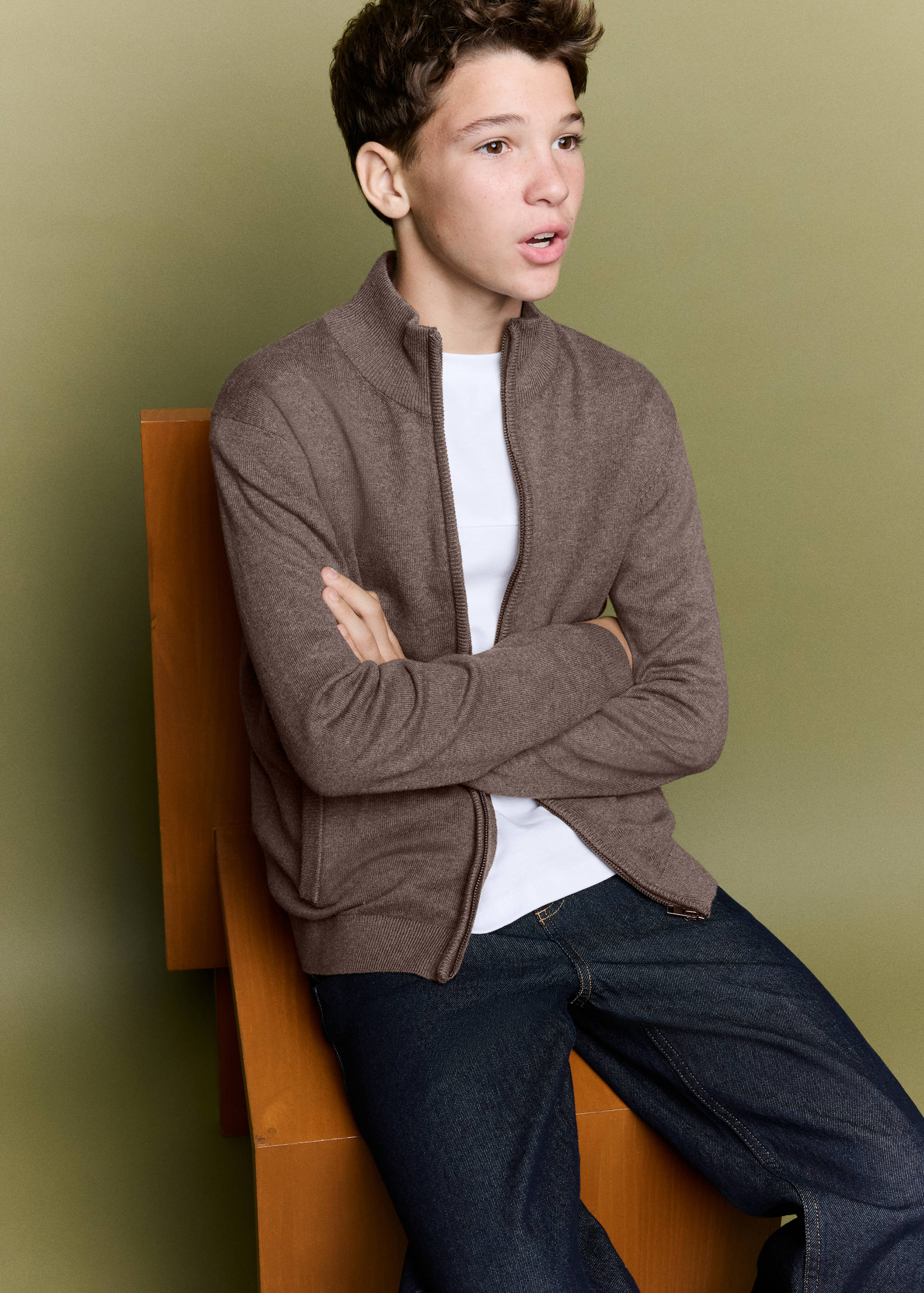 Brown knitted zip-up cardigan with high neck, worn with jeans.