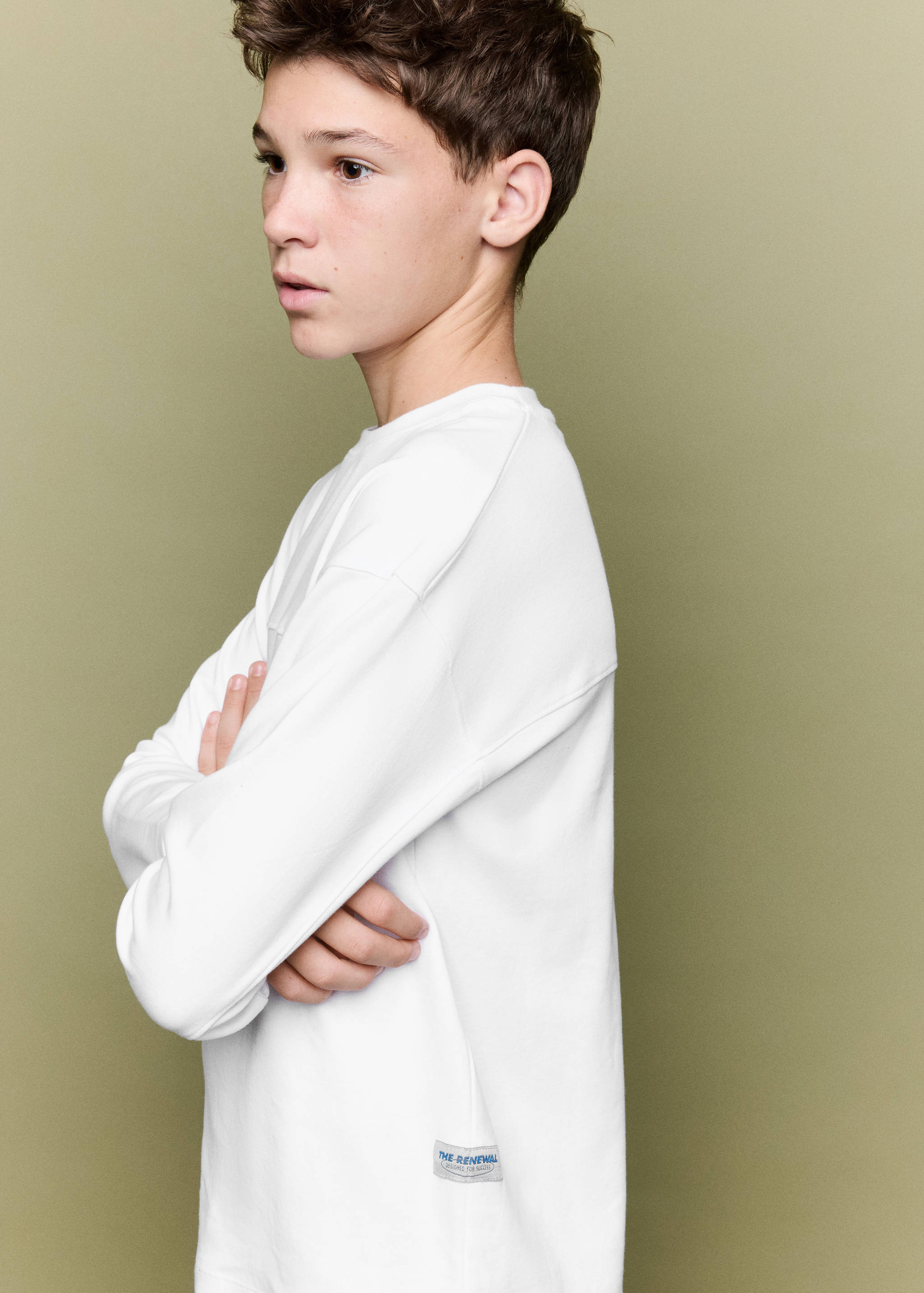 White long-sleeved t-shirt with a small hem label, worn by a model in profile.
