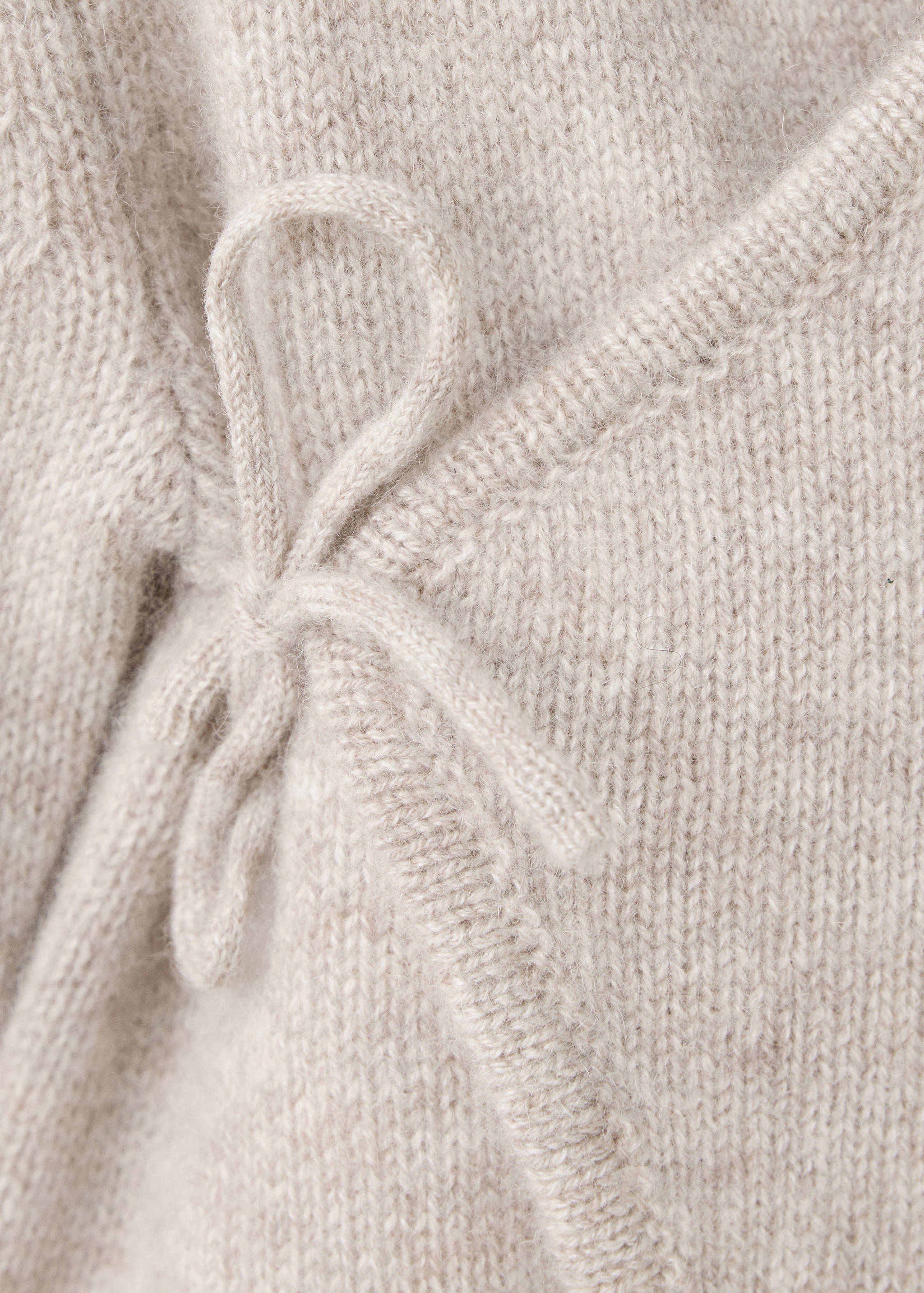 Close-up of a beige knit baby jumpsuit showing the side tie closure.