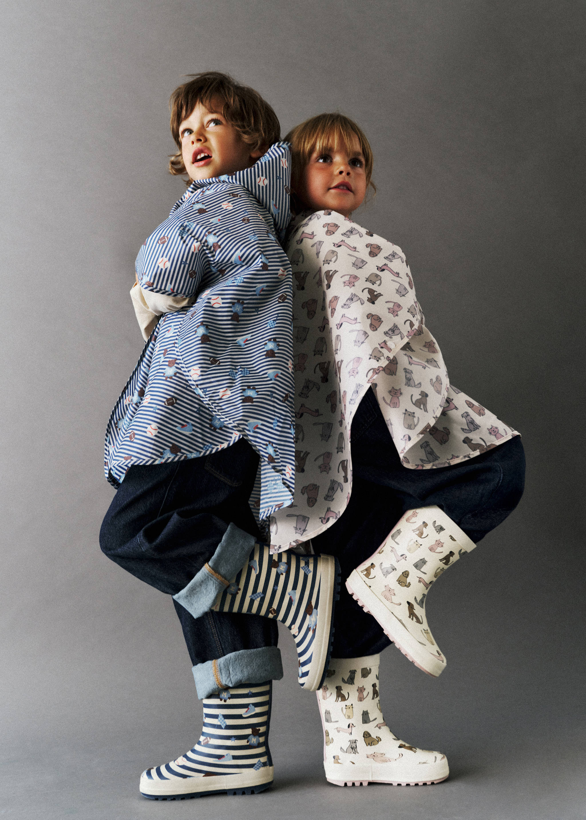 Kids' patterned rain boots worn by two children posing back-to-back.