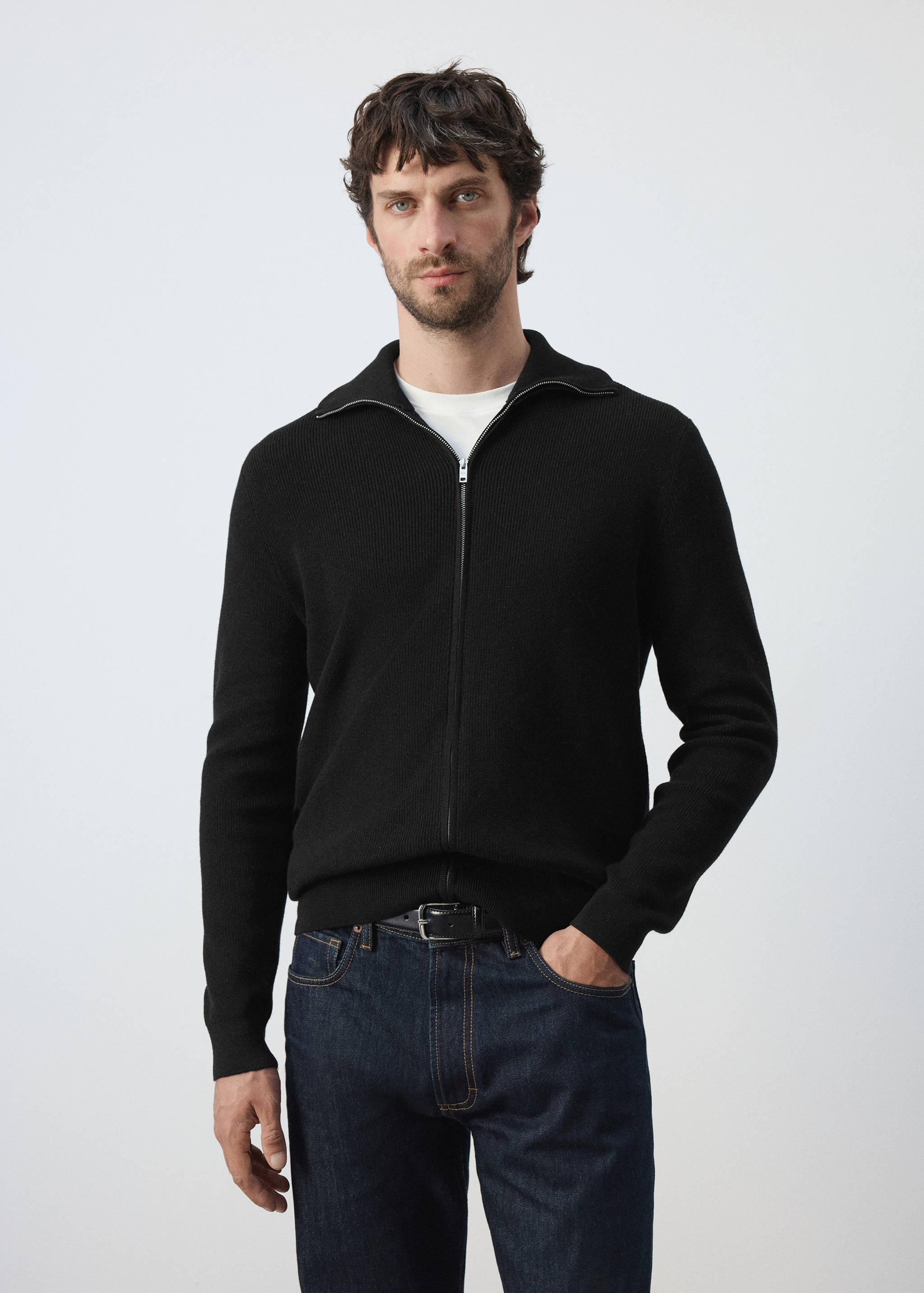 Black knitted zip-up cardigan with a collar worn over a white t-shirt.