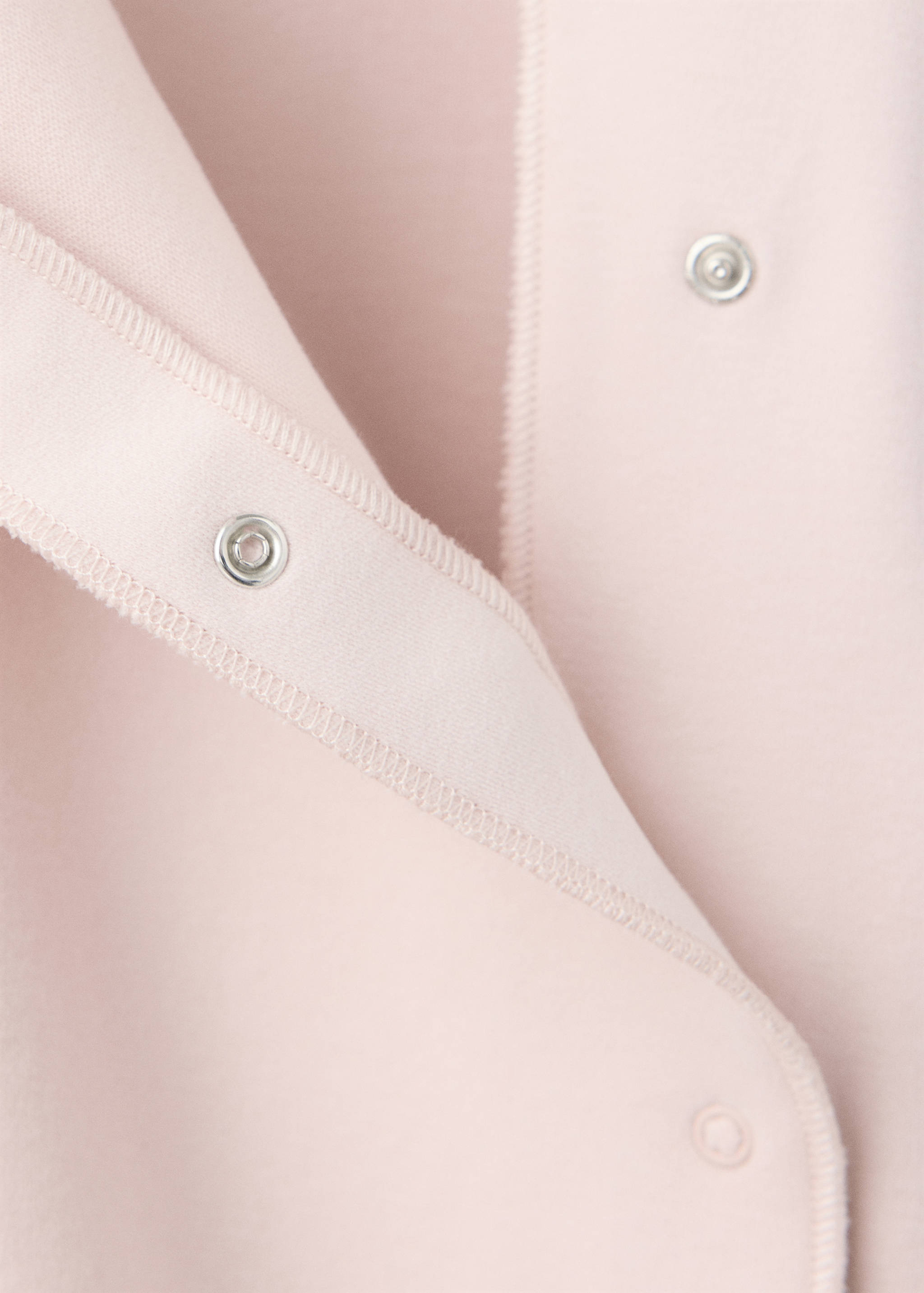 Pink baby pyjama jumpsuit detail showing snap button fastening.