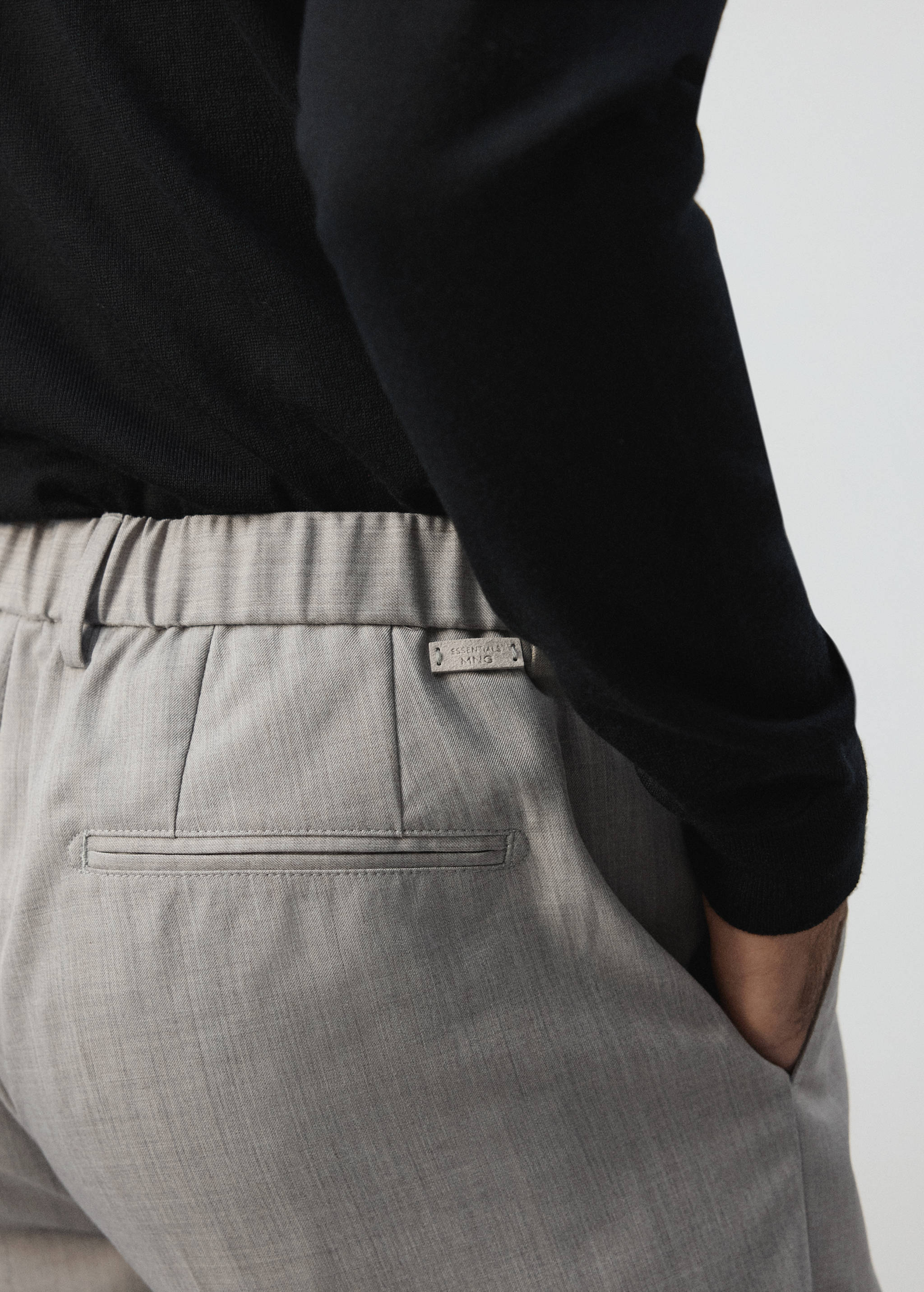 Close-up of light grey trousers with an elasticated waistband and welt pocket.