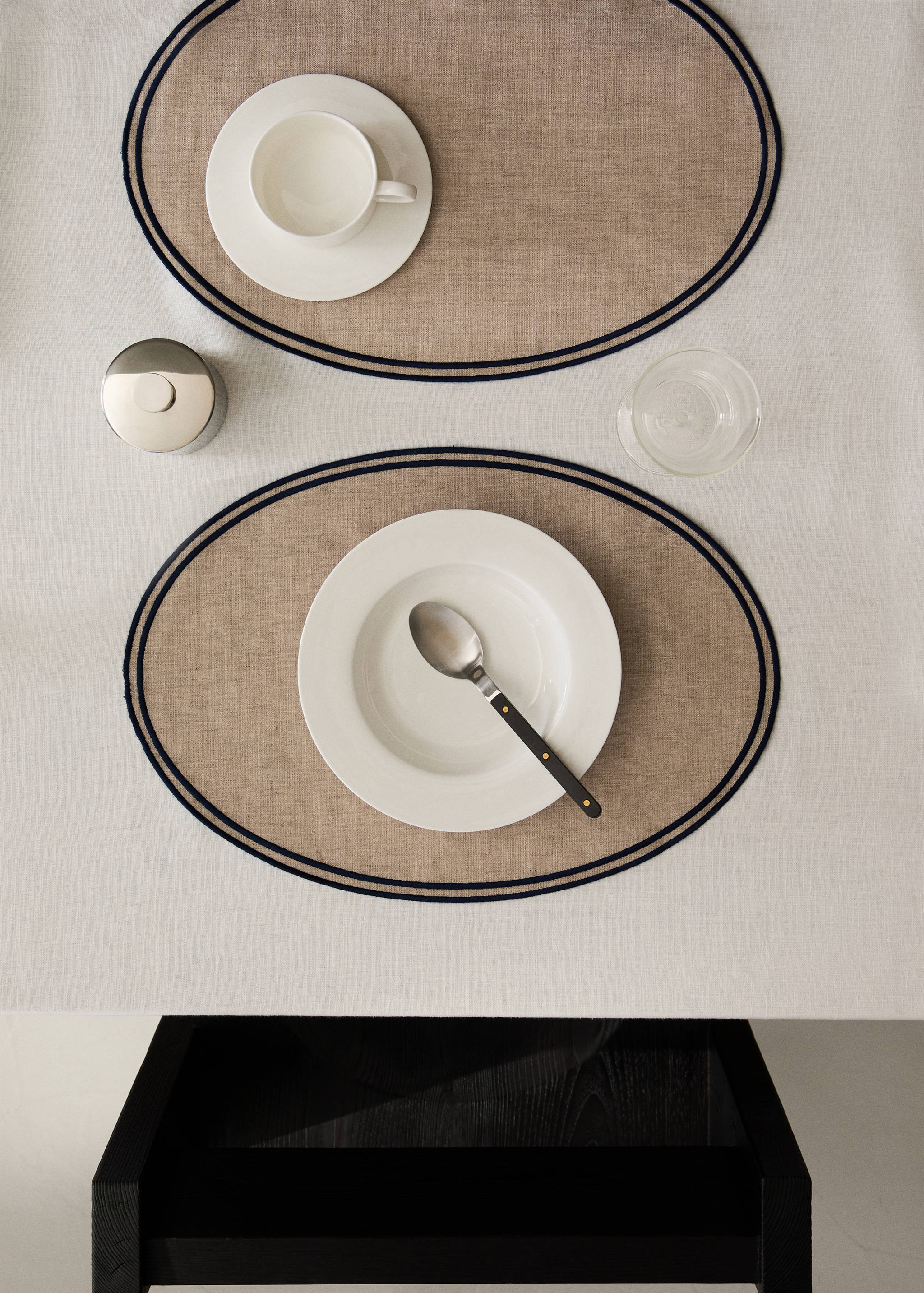 Oval beige placemats with a double navy blue border.