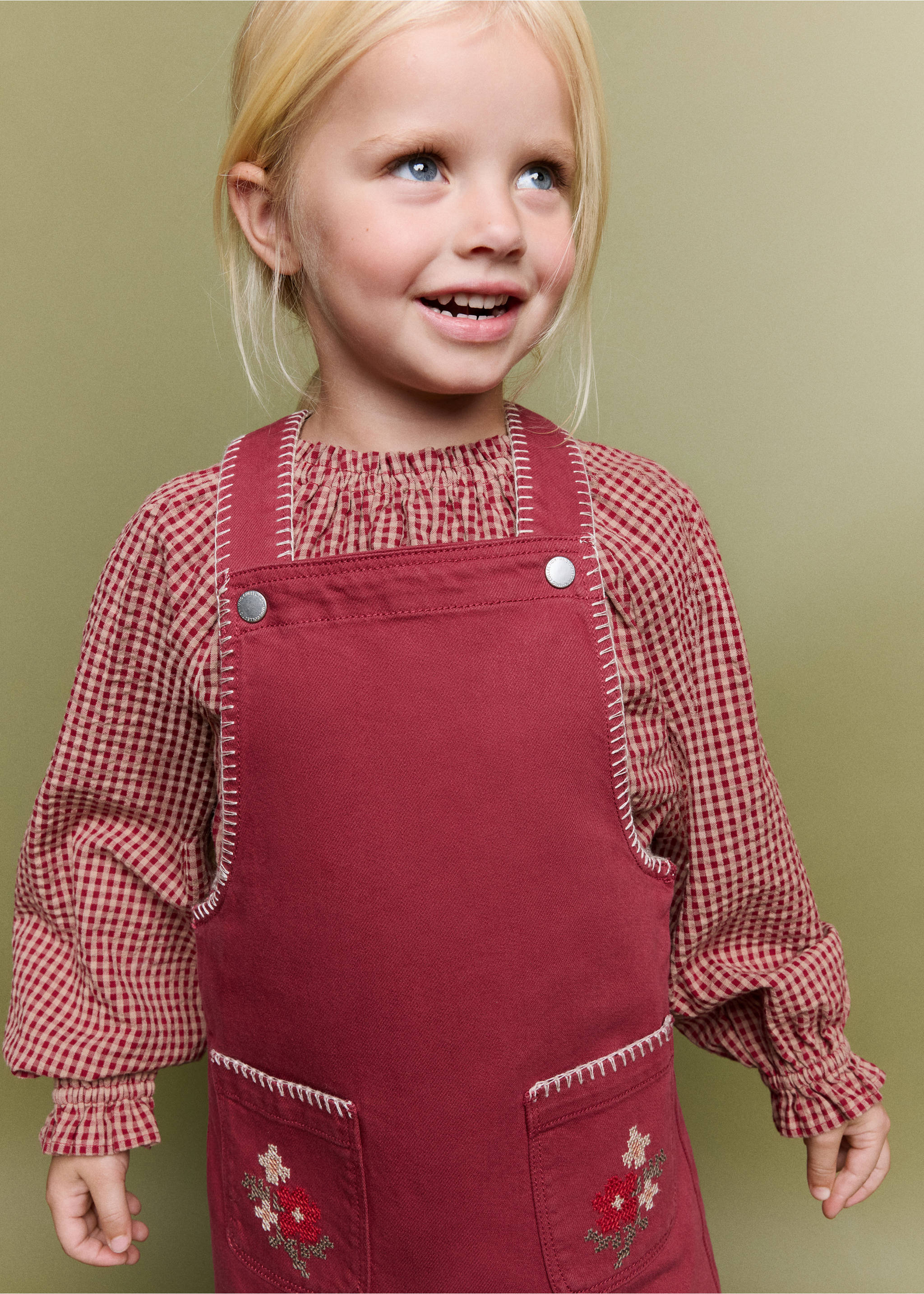 Burgundy pinafore dress with contrast embroidery, worn over a gingham blouse., Red. Ref: 37066344-00.