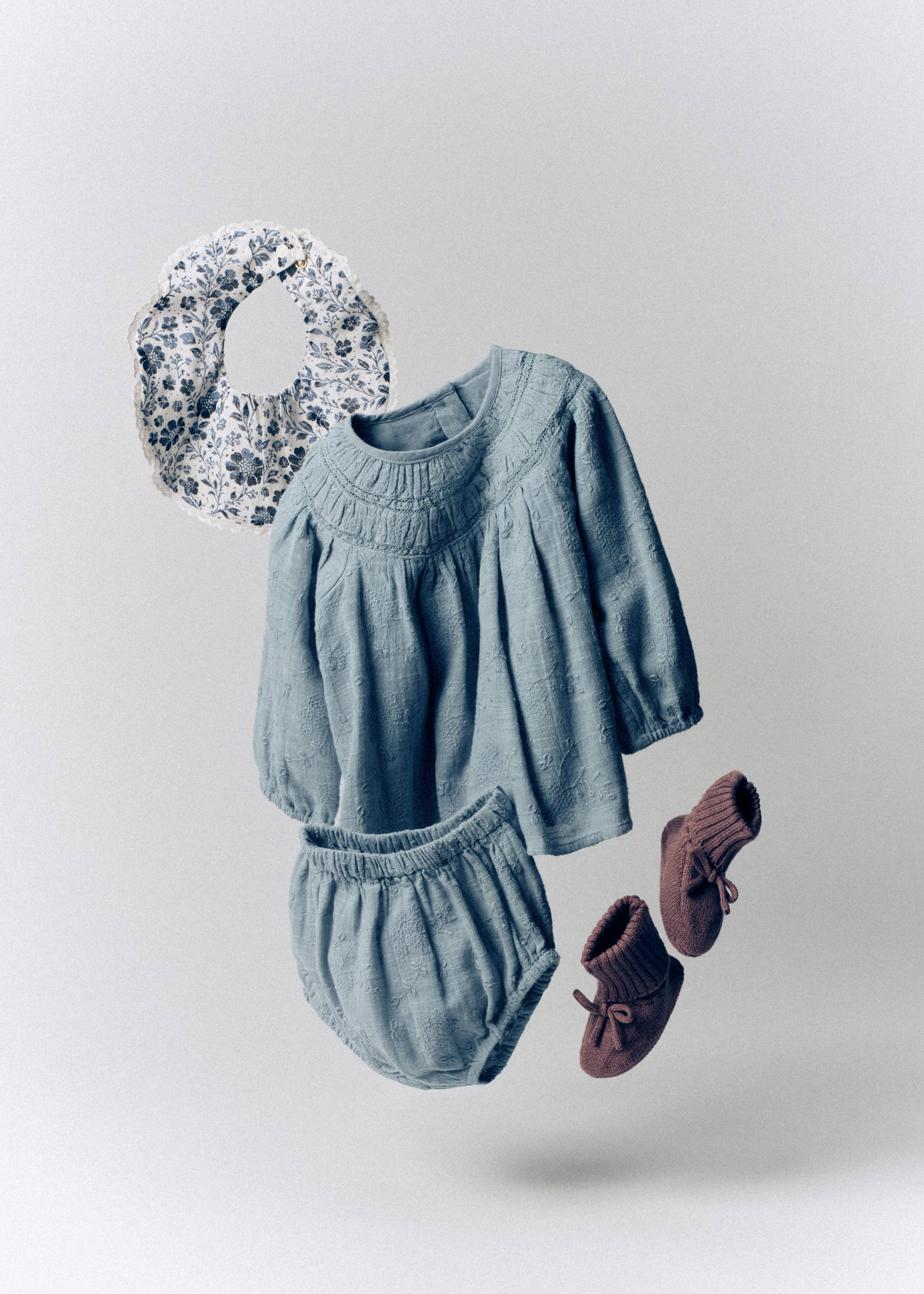 Pale blue long-sleeved dress with smocked yoke, matching bloomers, floral bib, and brown booties.