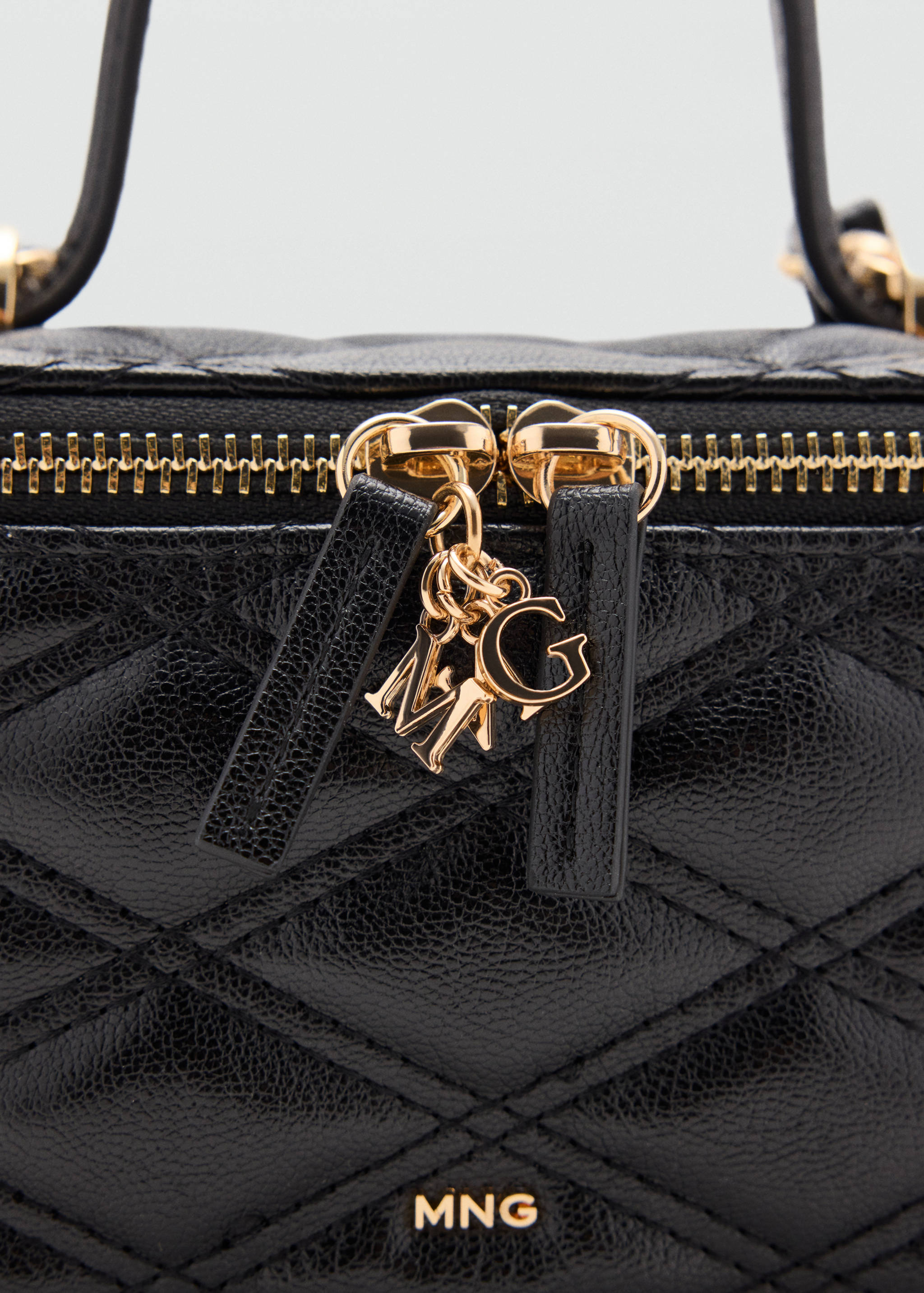Close-up of a black quilted vanity case with gold-tone MG charms and zip closure.