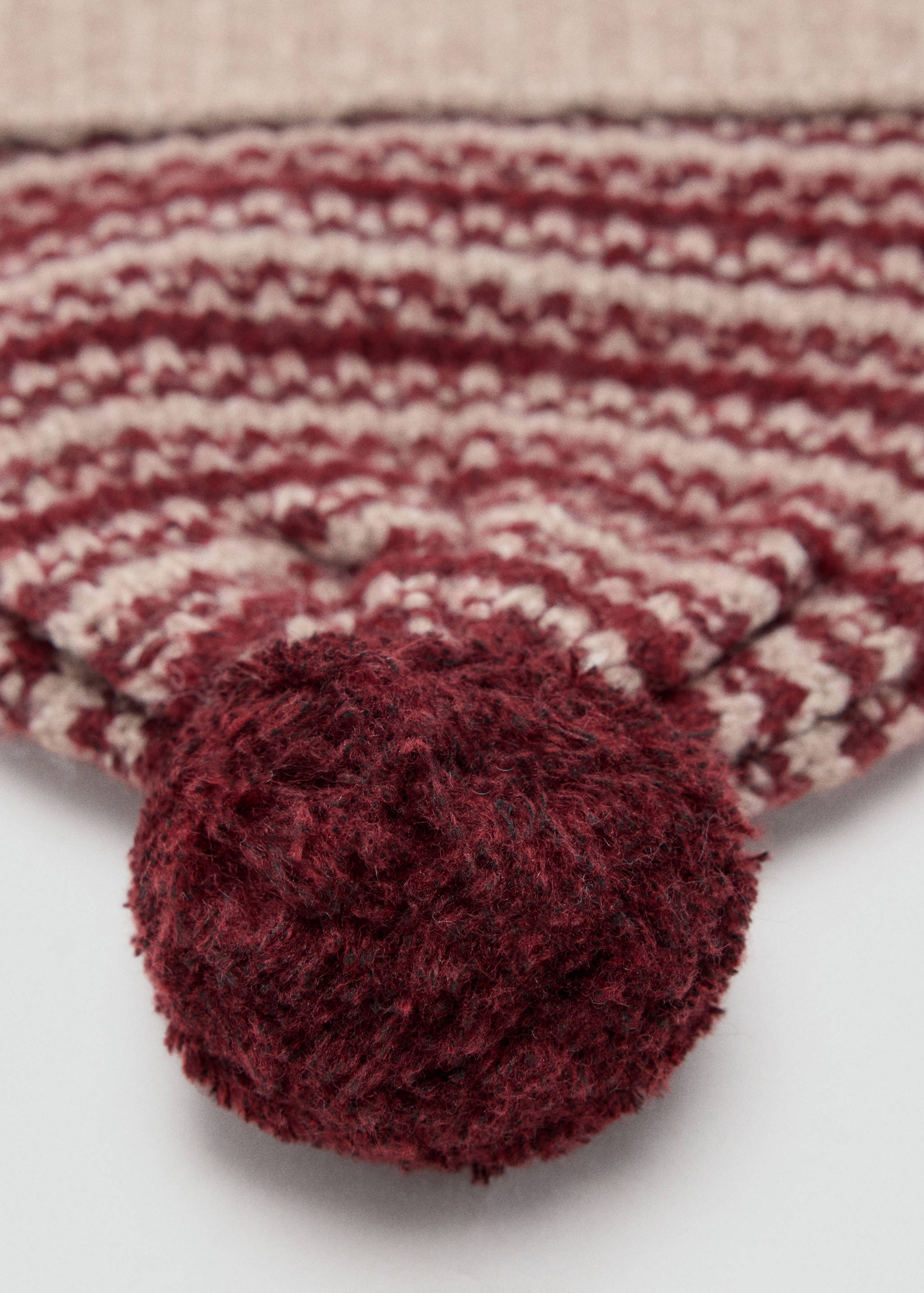 Close-up of a burgundy and beige patterned knit beanie with a pom-pom.