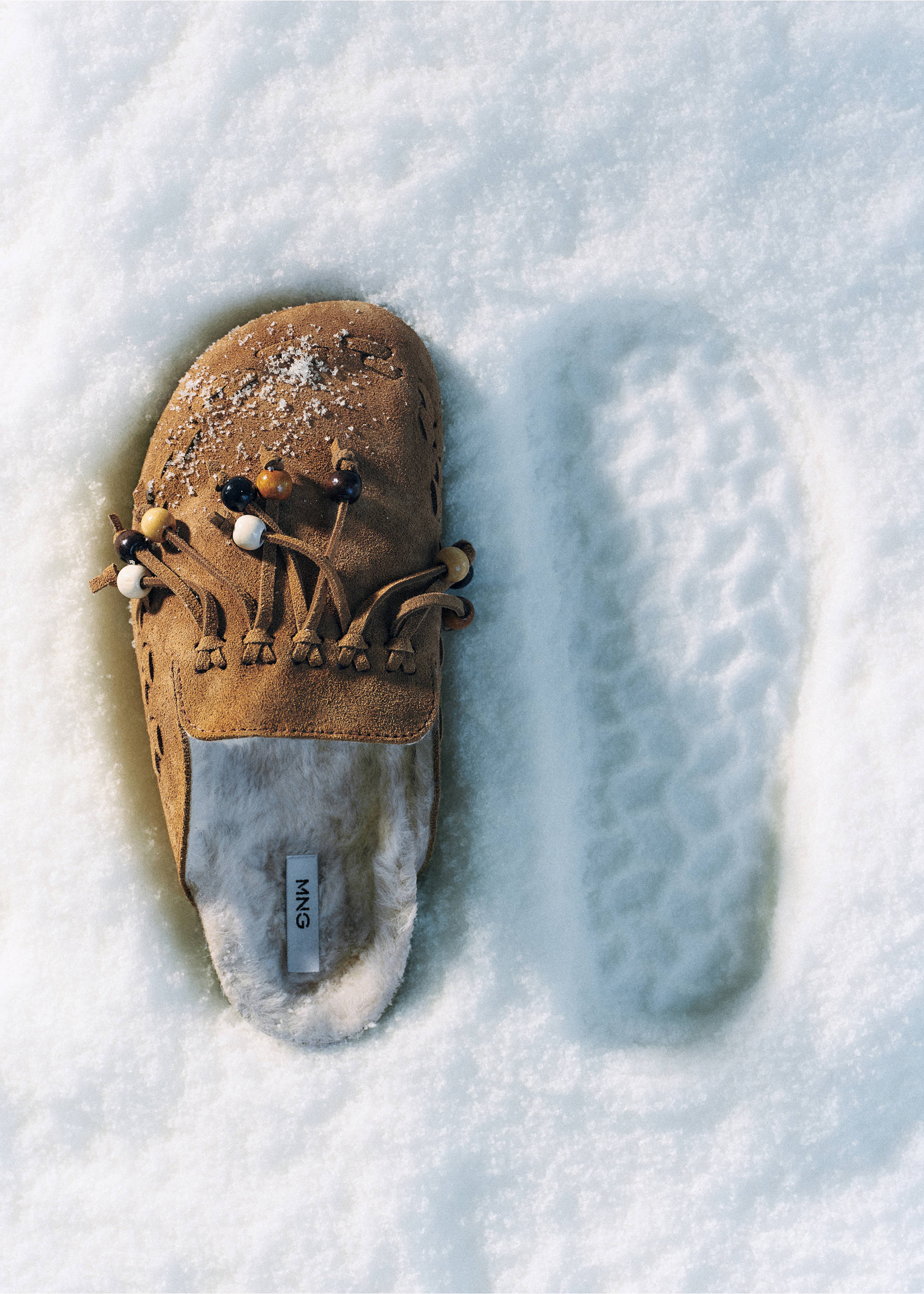 Brown suede shoe with fringing, wooden beads, and a white faux-fur lining, resting on snow., Medium Brown. Ref: 37066369-00.