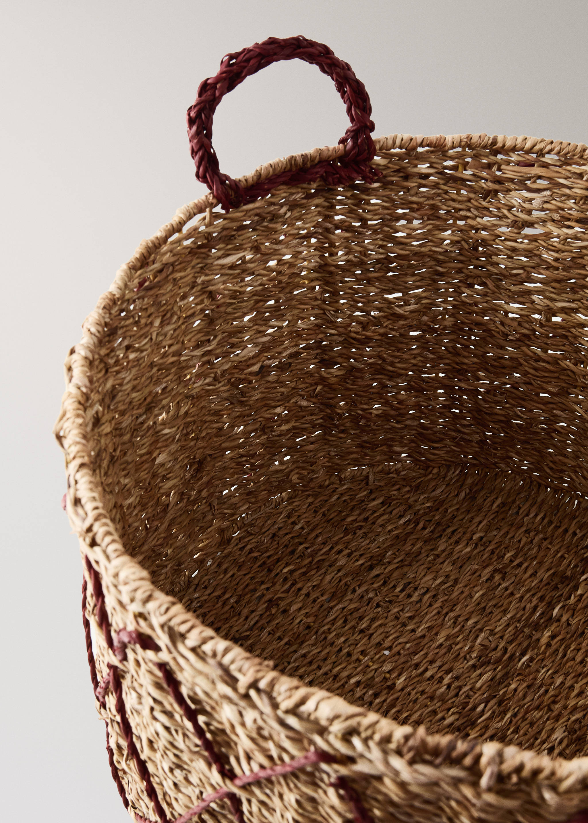 Close-up of a woven wicker basket with dark red braided handles.