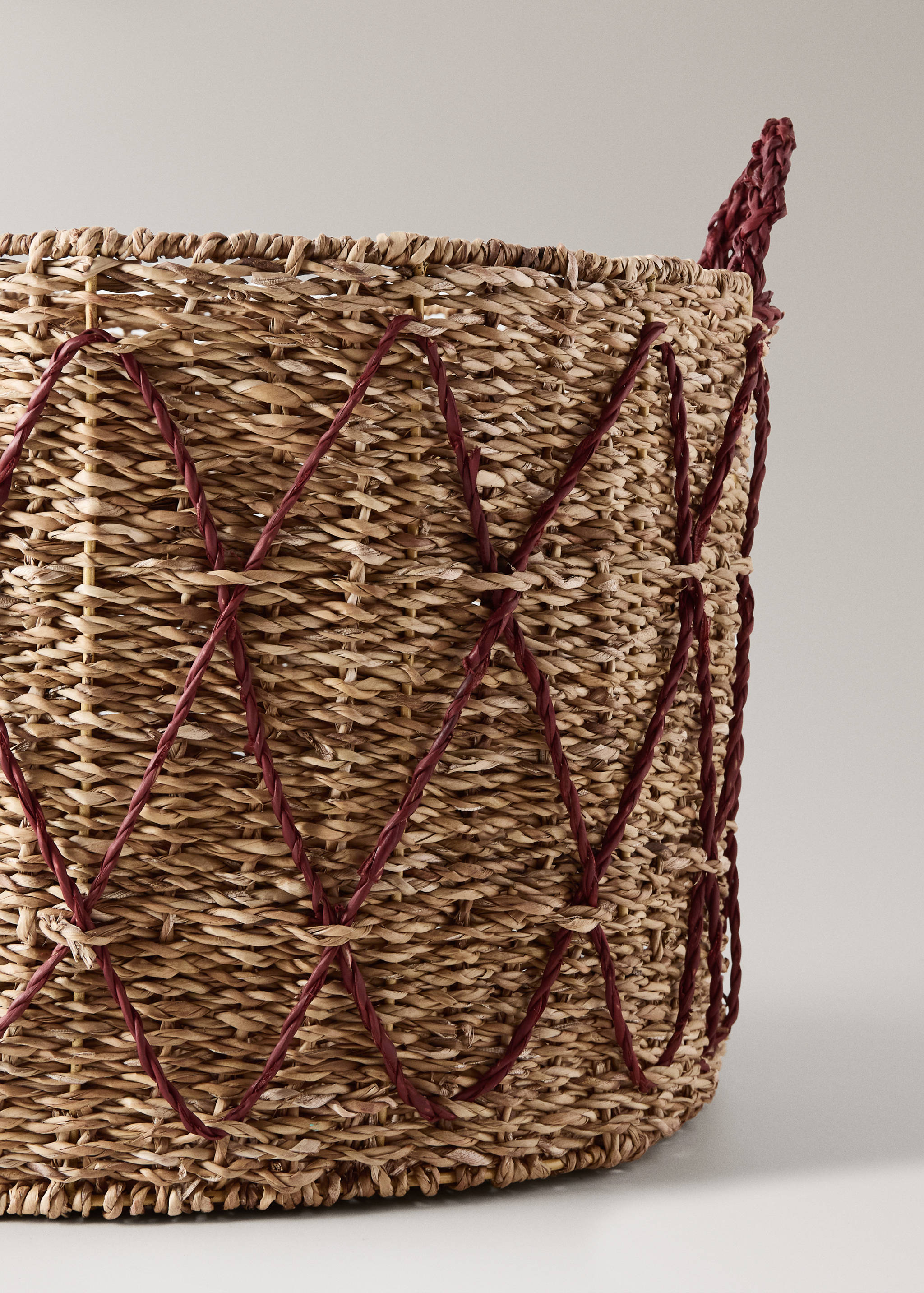 Close-up of a woven wicker basket with a burgundy diamond thread pattern.