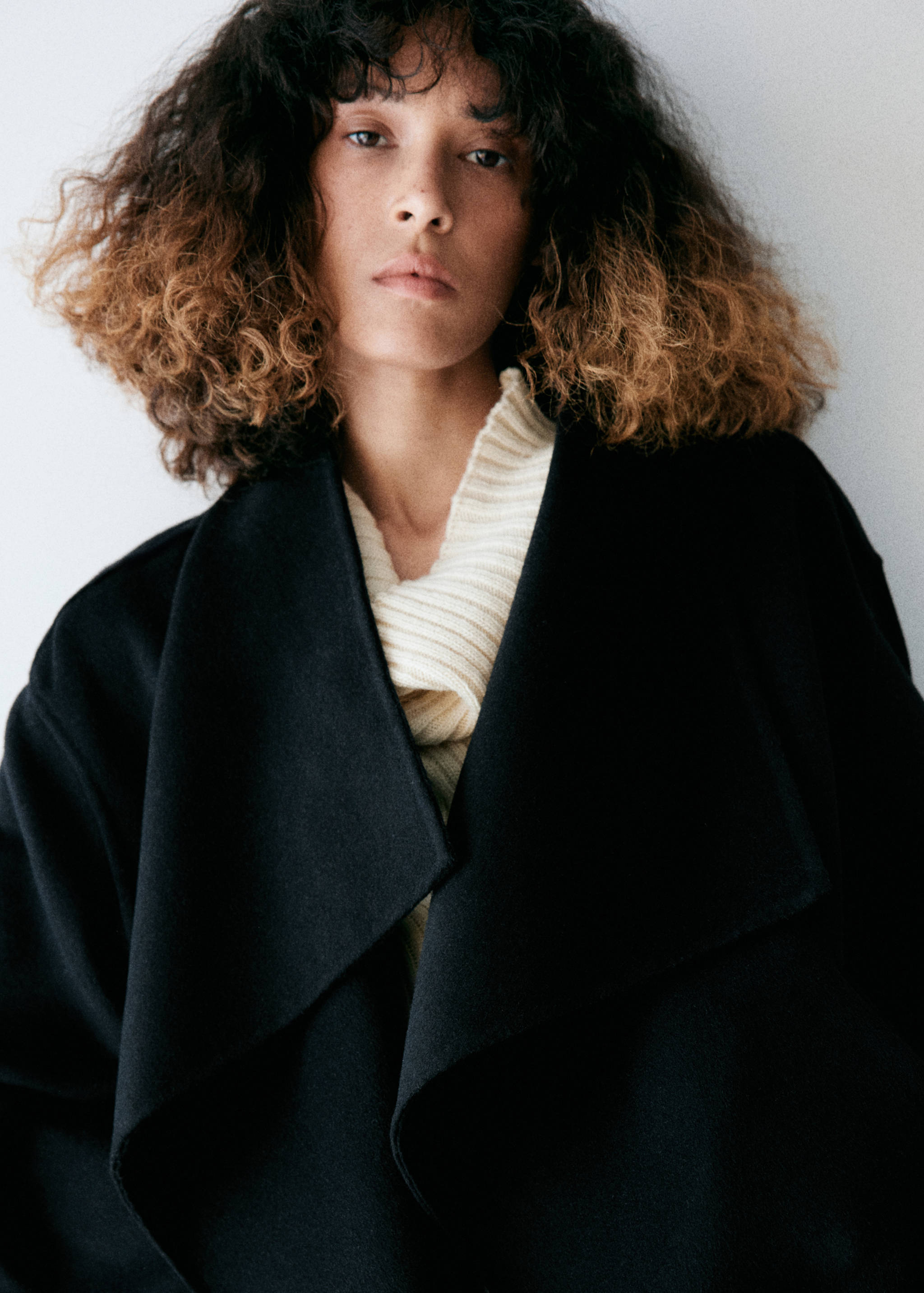 Close-up of a black jacket with wide lapels worn over a cream ribbed sweater.