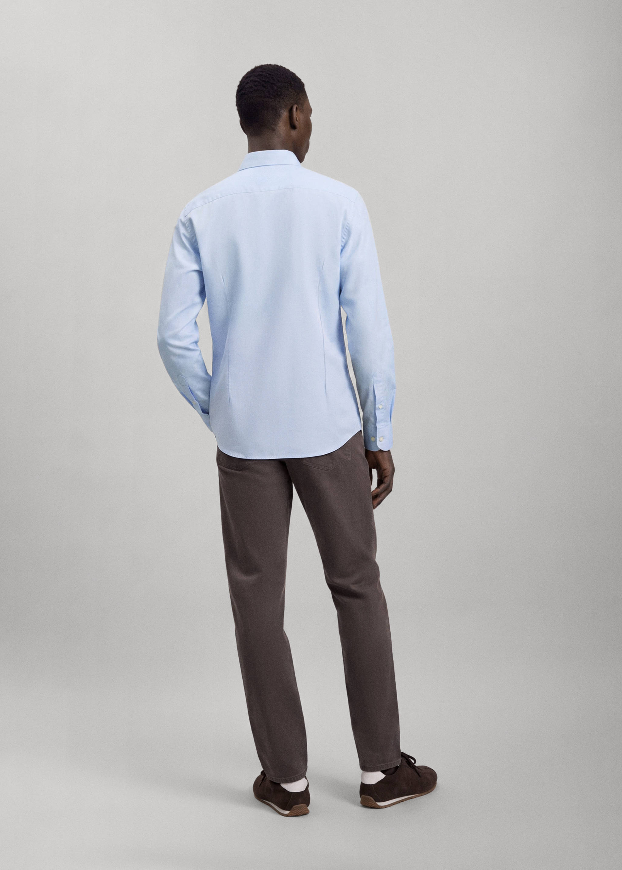 Back view of a light blue long-sleeved shirt worn with dark trousers.