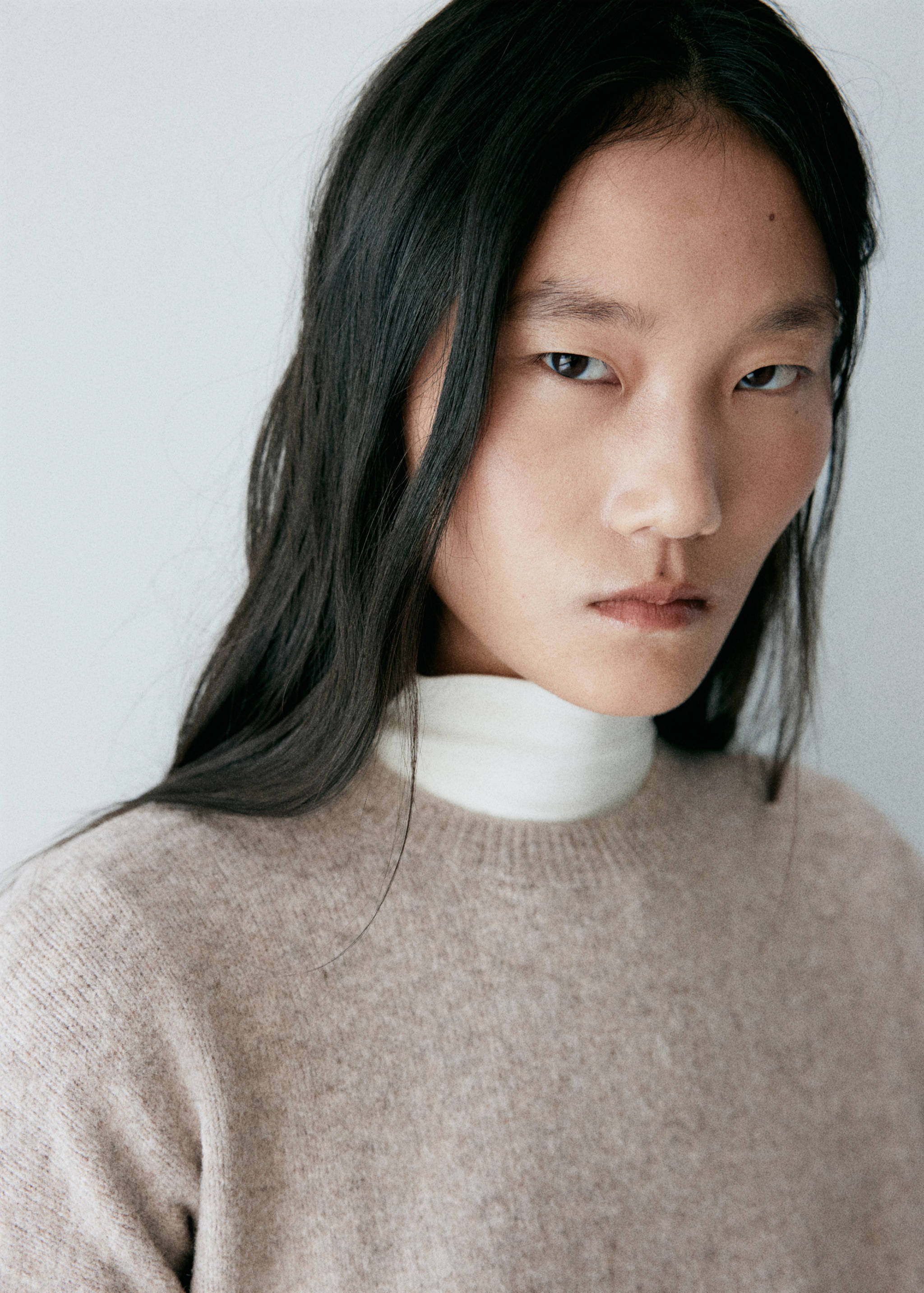 Close-up of a model wearing a beige knitted dress with a crew neck.