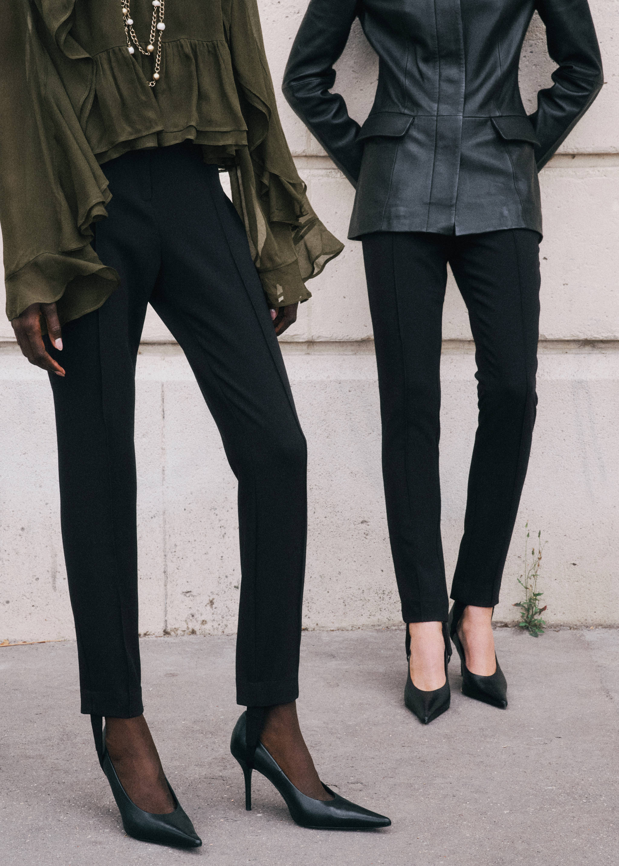 Black slim-fit trousers with front center seams, worn with an olive ruffled blouse and black heels.