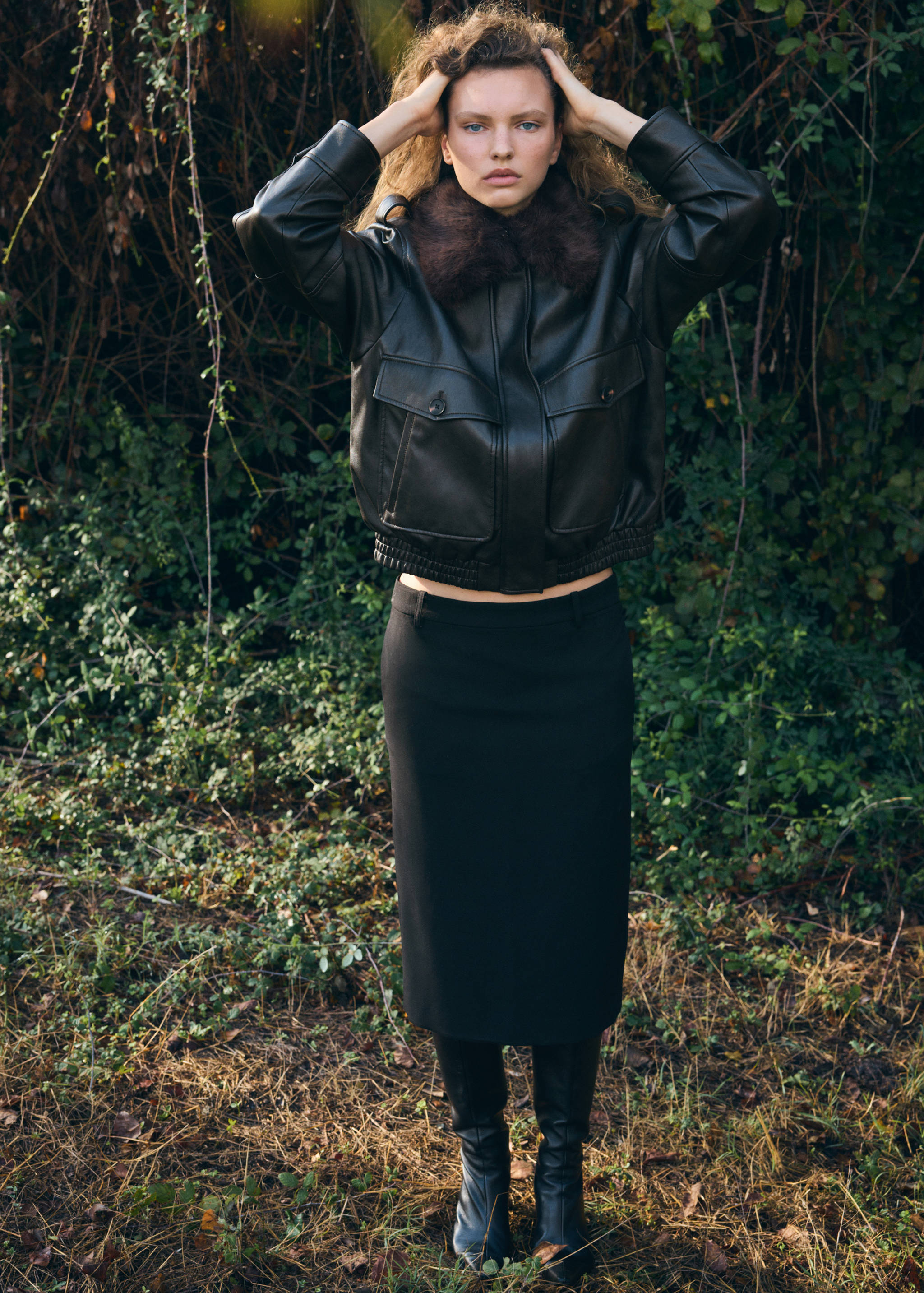 Dark brown faux-leather jacket with faux-fur collar, worn with a black midi skirt.