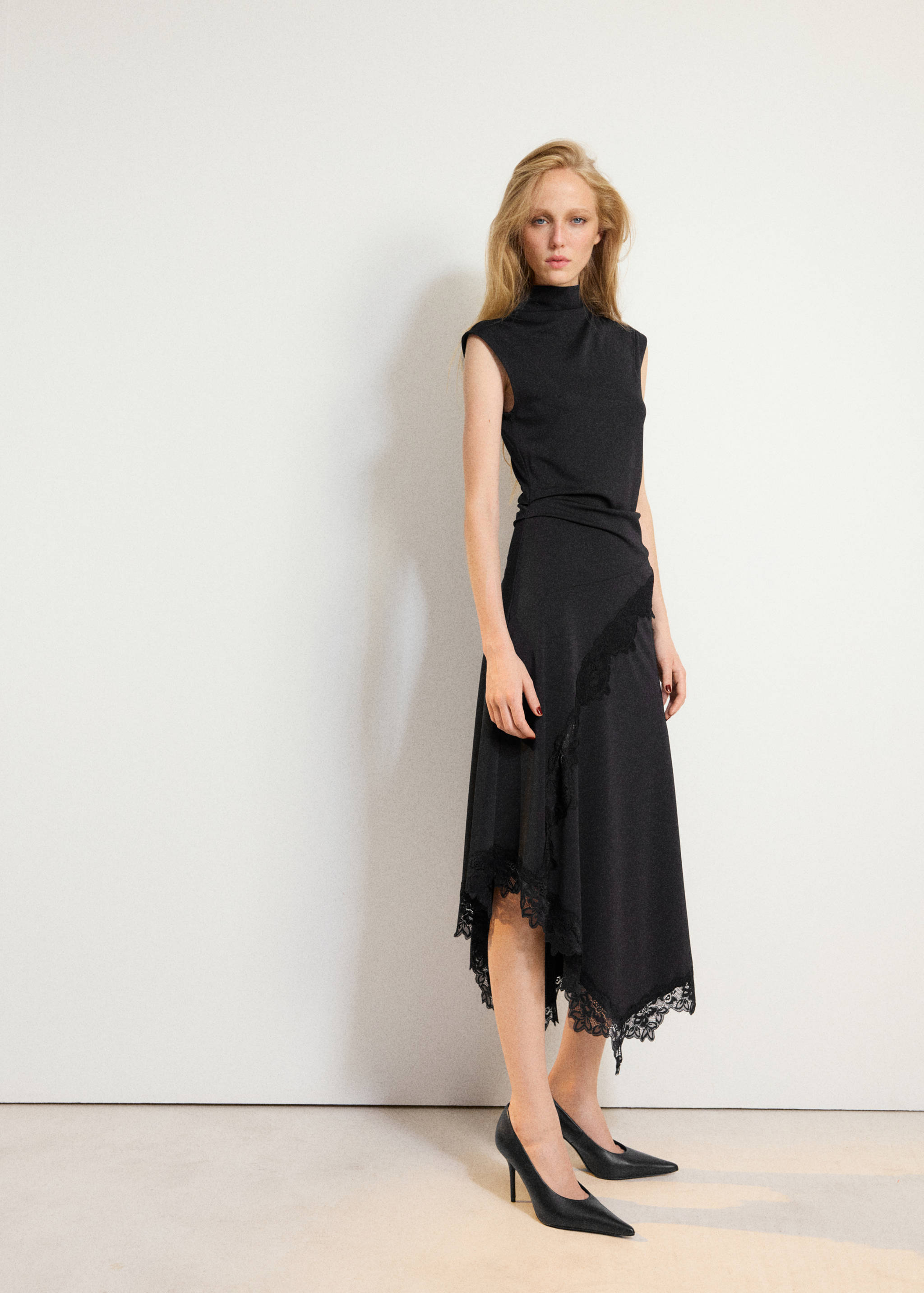 Vestido midi negro sin mangas con cuello alto y bajo asimétrico con detalles de encaje.