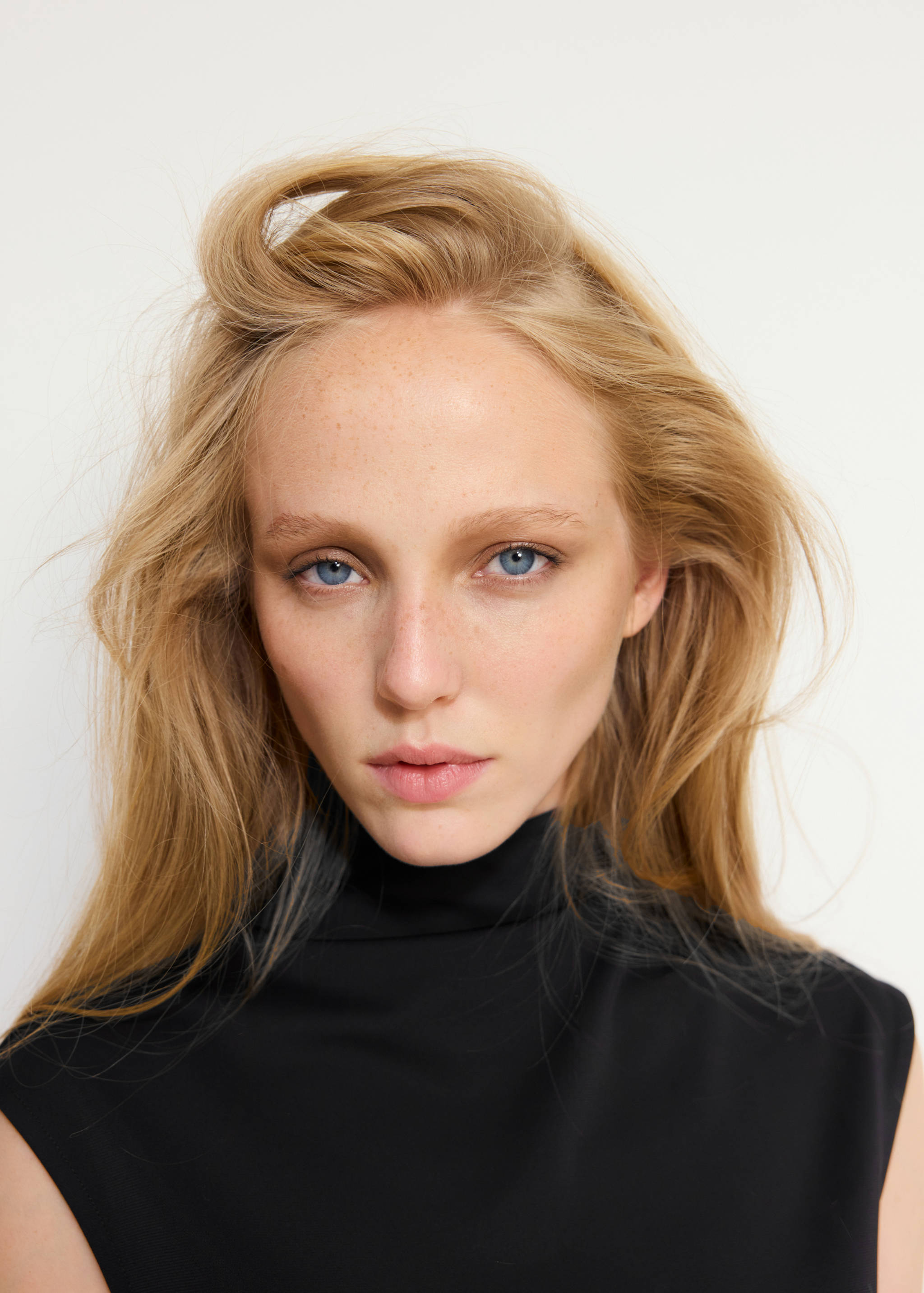 Primer plano de una modelo con vestido negro sin mangas y cuello alto.