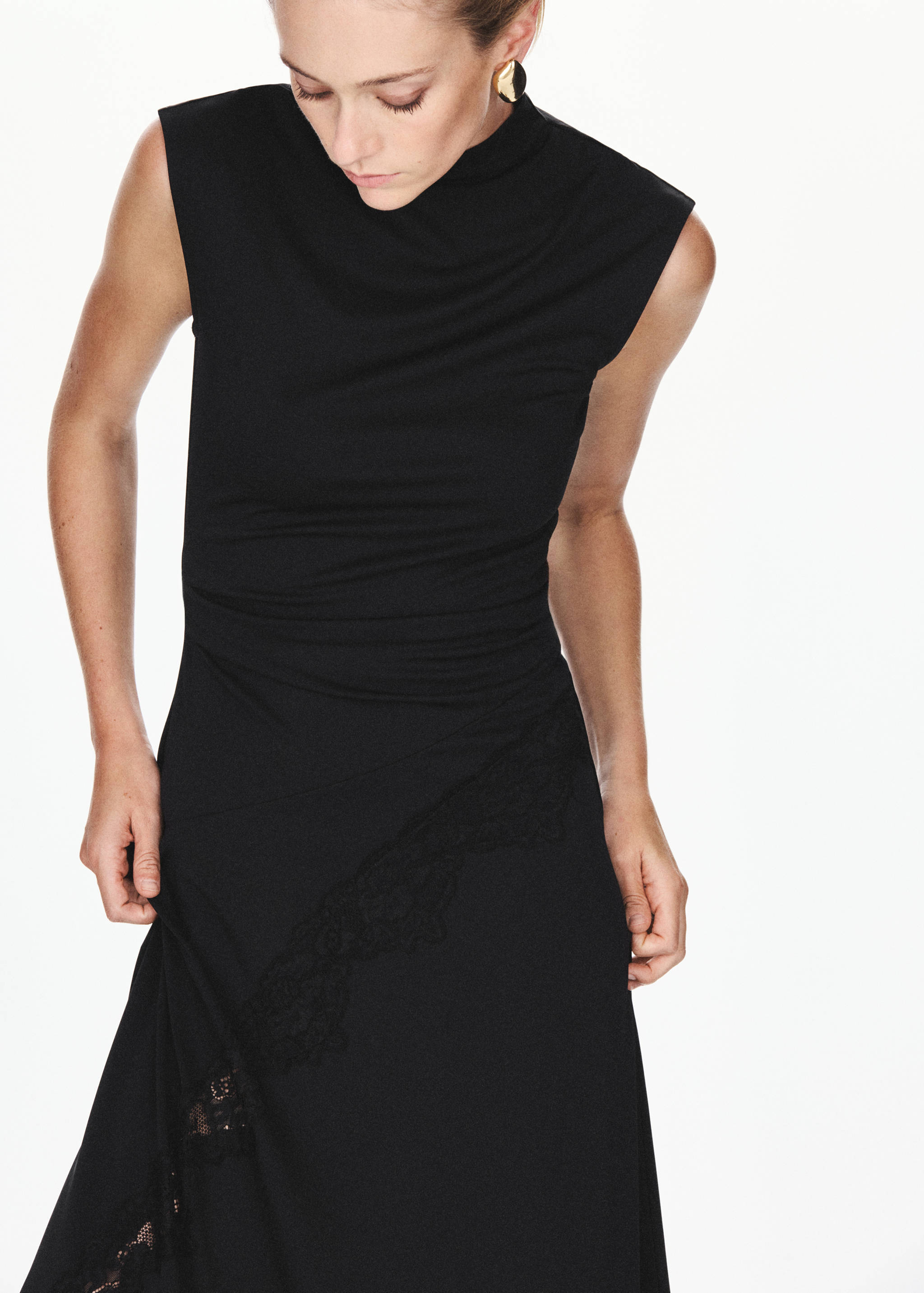 Black sleeveless dress with a high neck, fitted waist, and diagonal lace trim.