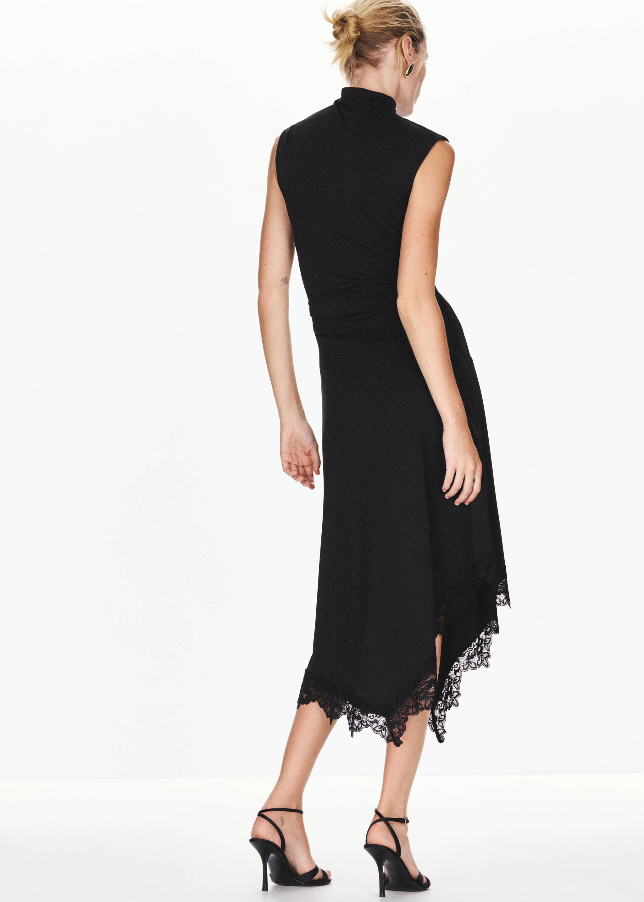 Back view of a black sleeveless midi dress with a high neck and lace-trimmed asymmetrical hem.