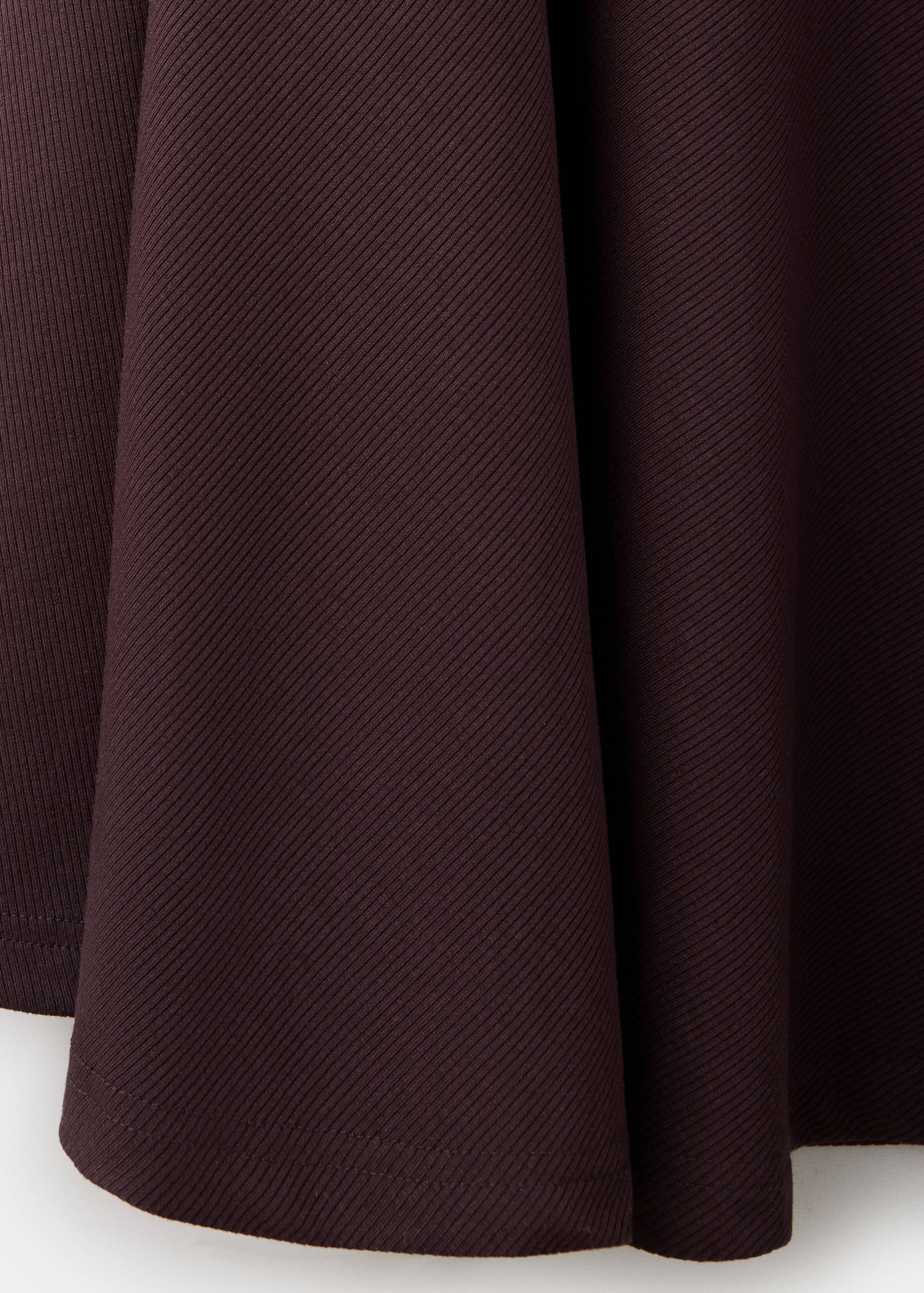 {
    "extended_description": "This is a close-up texture shot of a dark brown or plum-coloured ribbed dress, showing the fine diagonal ribbing and soft drape of the fabric in folds.",
    "alt_text": "Close-up of the dark brown ribbed fabric
 texture on a dress."
}