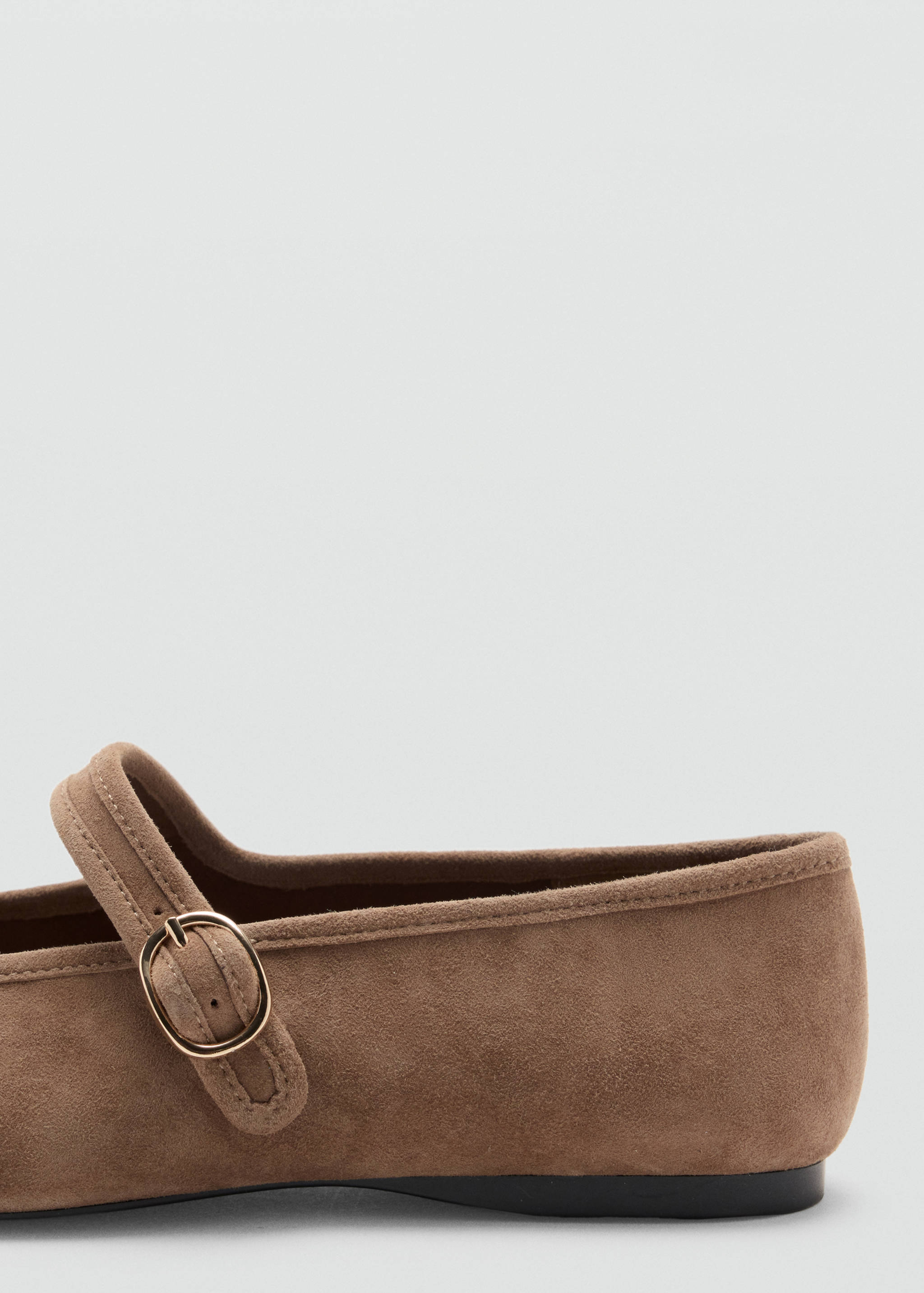 Brown flat shoe detail with a strap and metallic buckle.