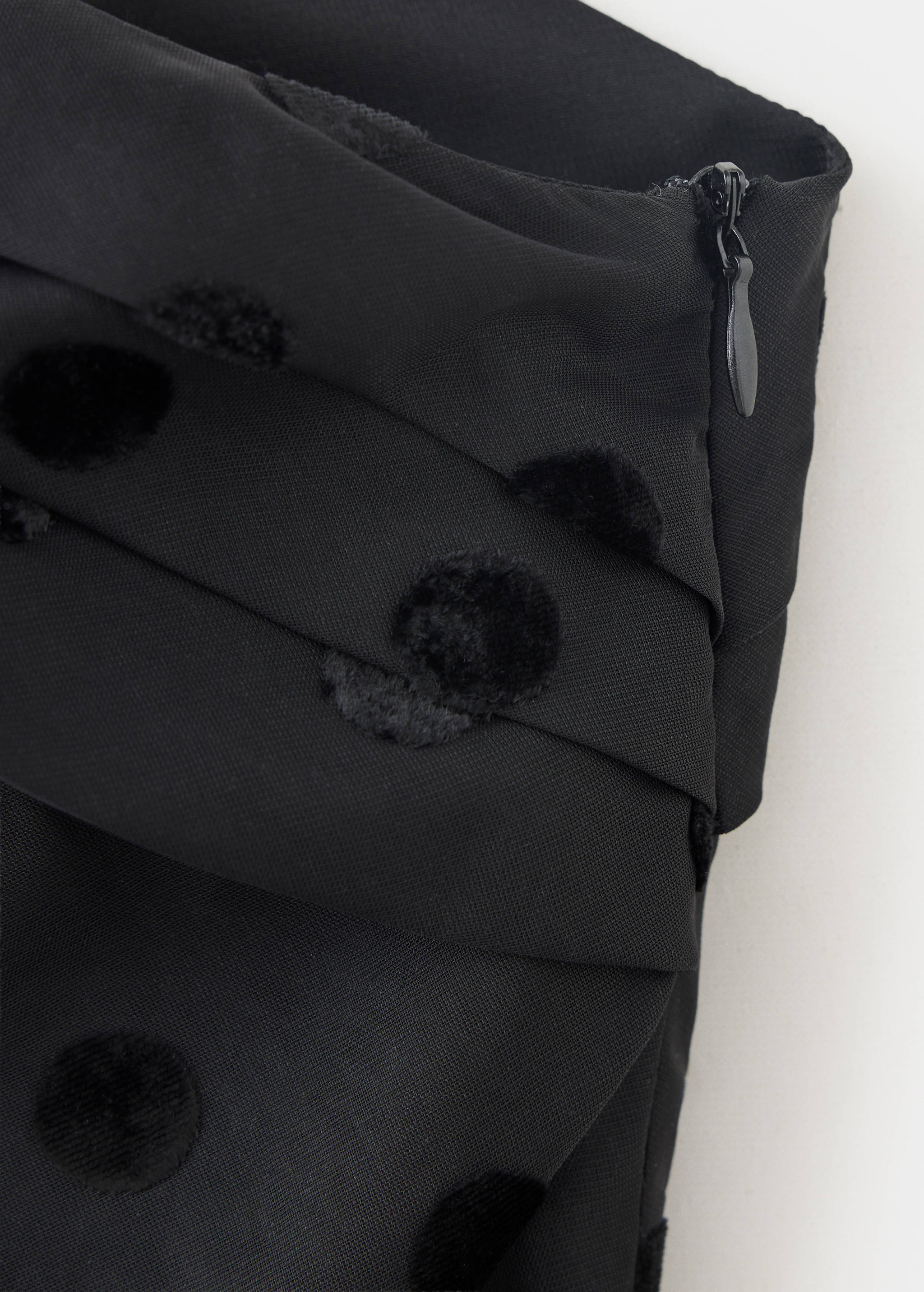 Close-up of a black top fabric with velvet polka dots and side zip.