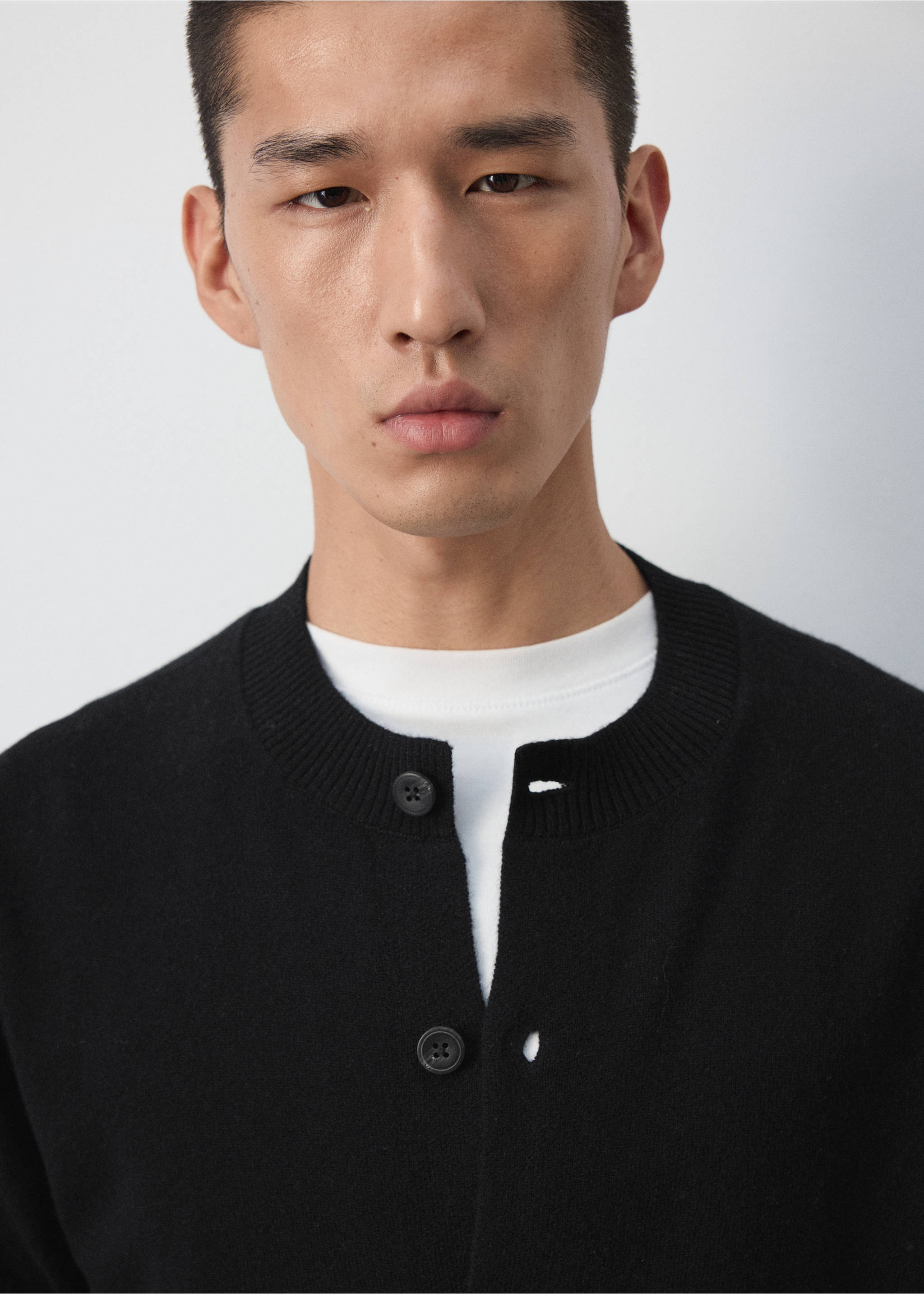 Close-up of a black cardigan with a round neckline and button fastening worn over a white t-shirt., Black. Ref: 37067886-00.