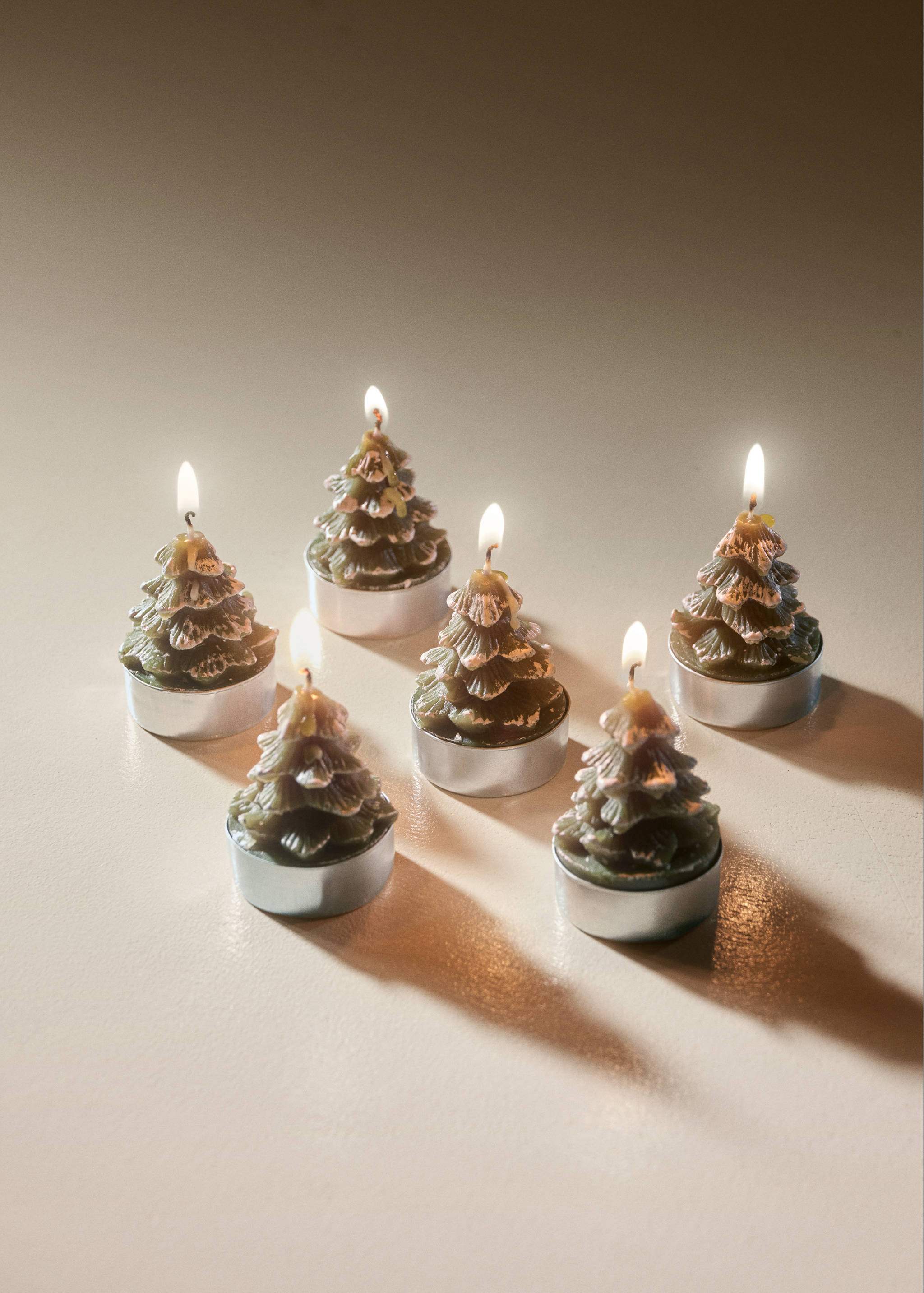 Set of six lit green Christmas tree-shaped candles in silver-colored metal bases.