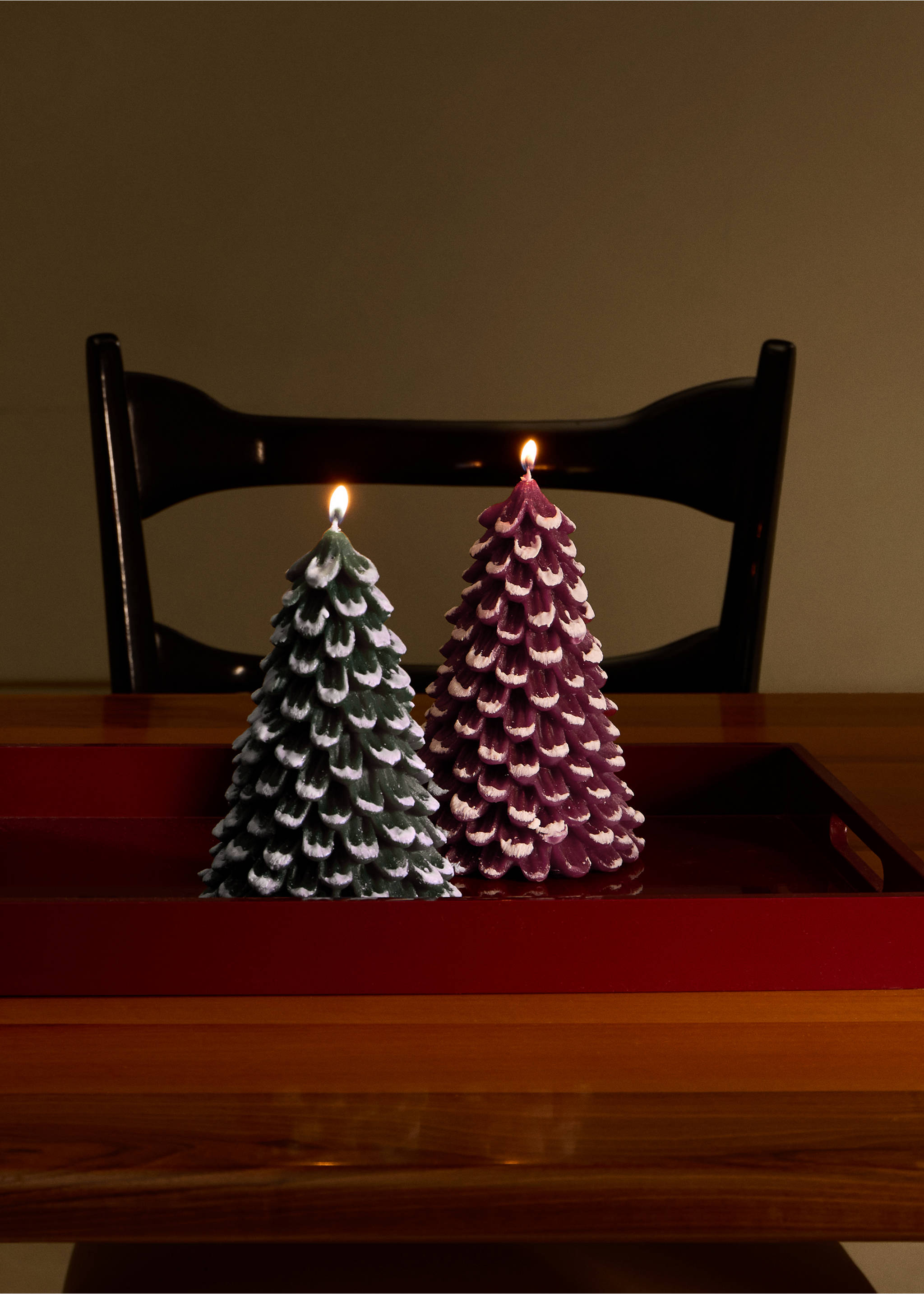 Two lit pine tree-shaped candles in green and purple on a red tray., Green. Ref: 37067892-00.
