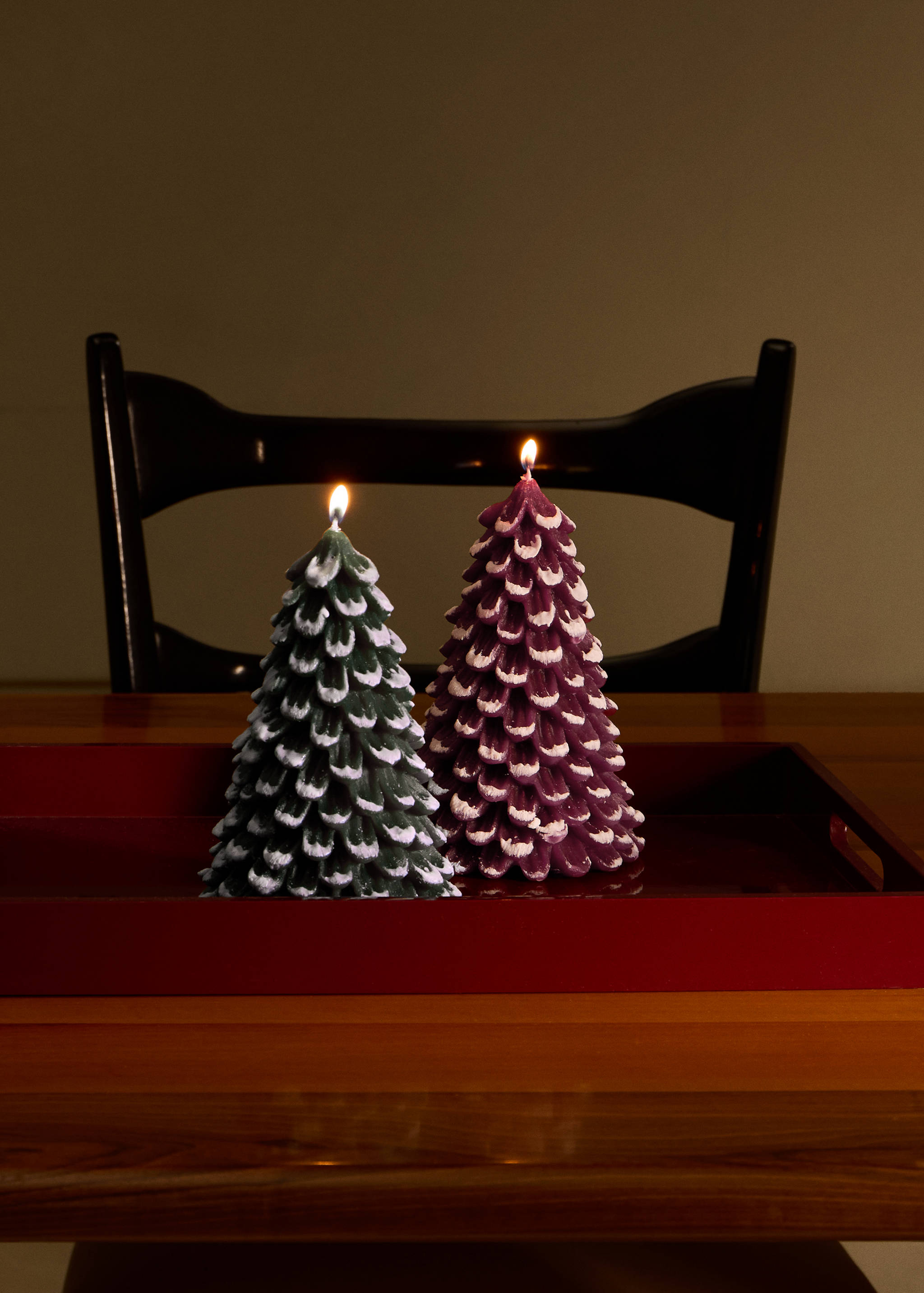 Two lit pine tree-shaped candles in green and purple on a red tray.