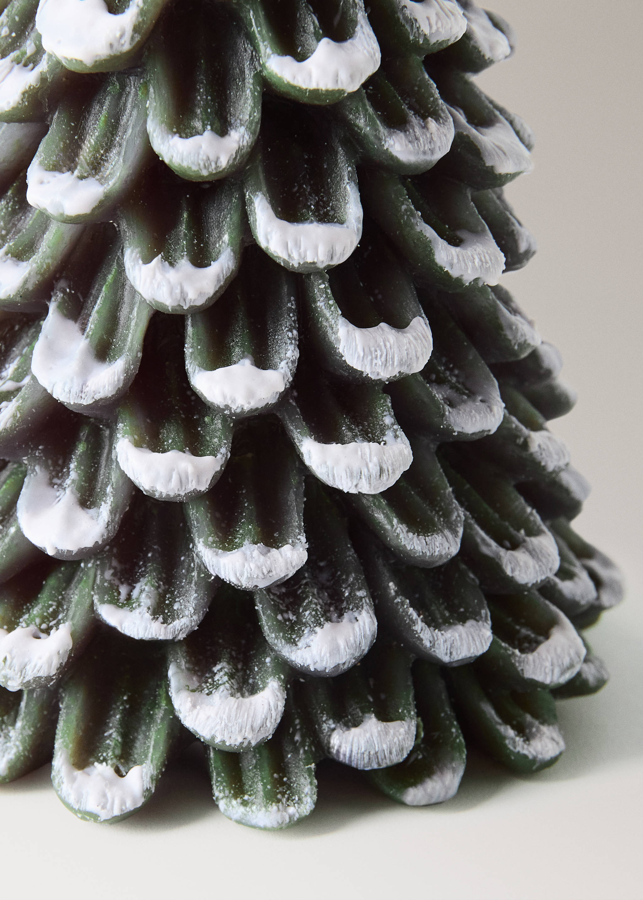 Close-up of a green pine tree candle with white wax on the tip of each branch.