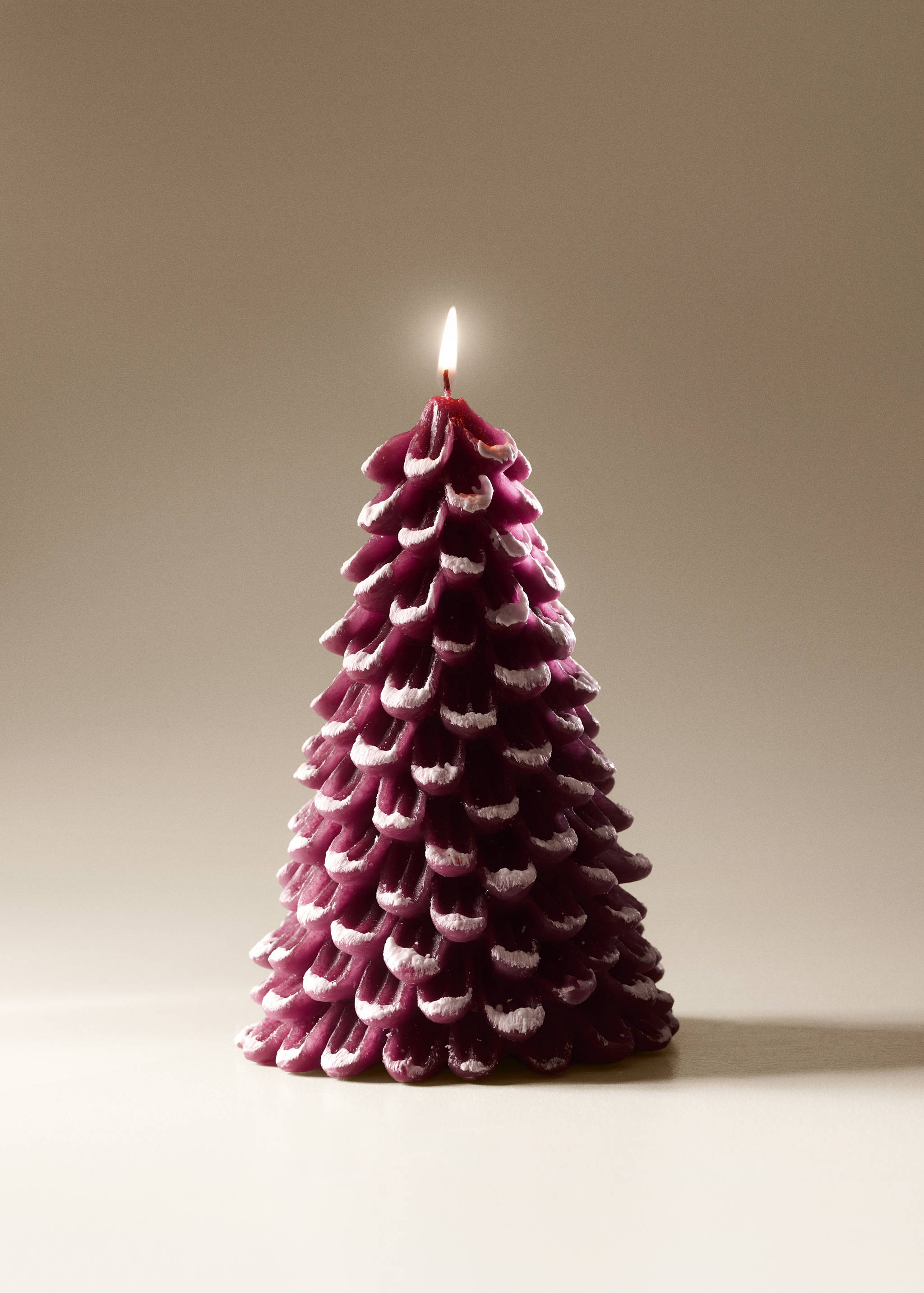 Dark purple tree-shaped candle with snow-effect white tips and a lit wick.