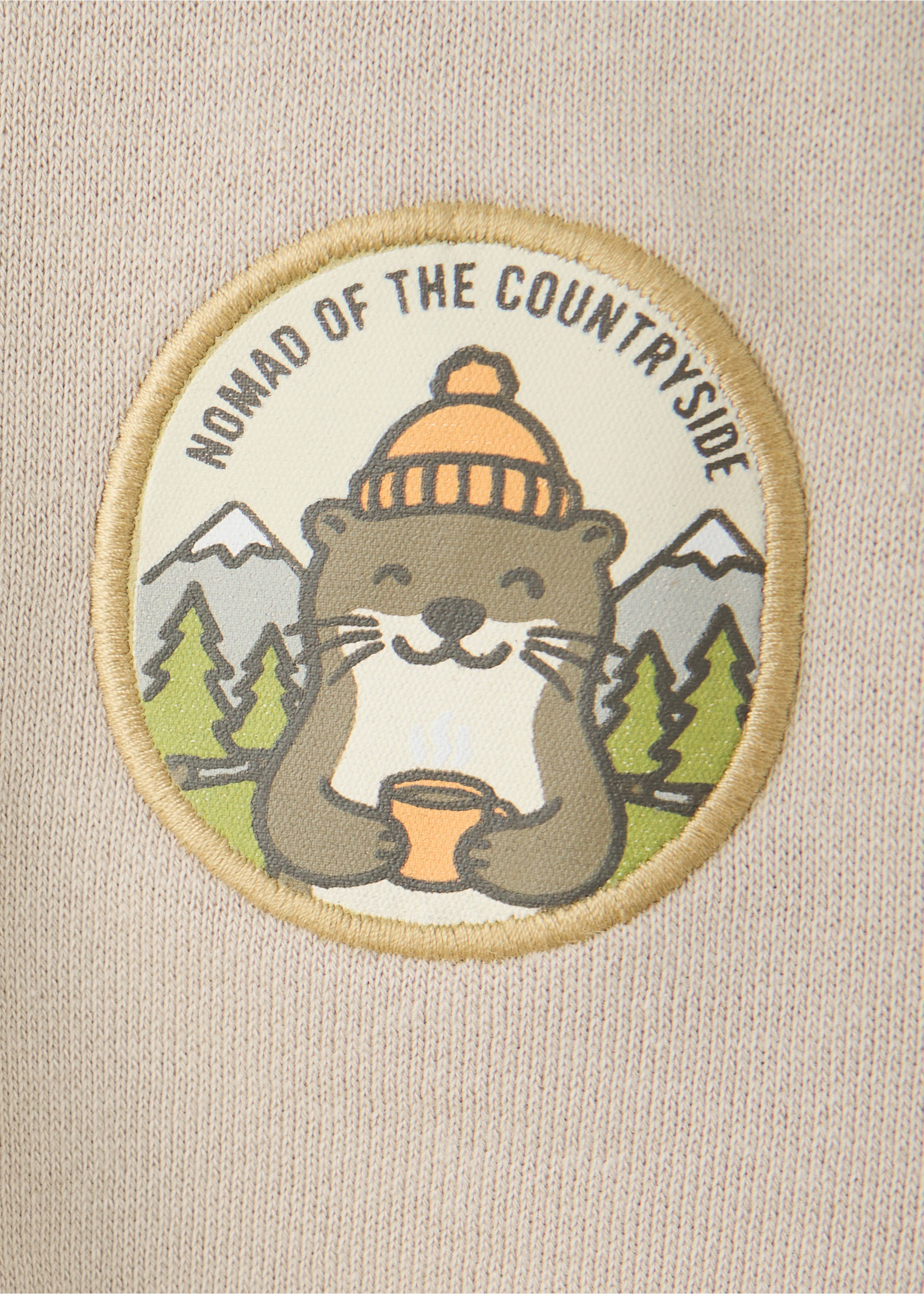 Beige sweatshirt fabric detail featuring a round otter patch with 'NOMAD OF THE COUNTRYSIDE' text., Sand. Ref: 37067907-00.